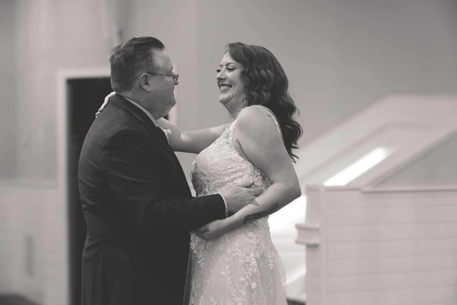 A couple shares a joyful moment together in black and white during what appears to be a wedding celebration.