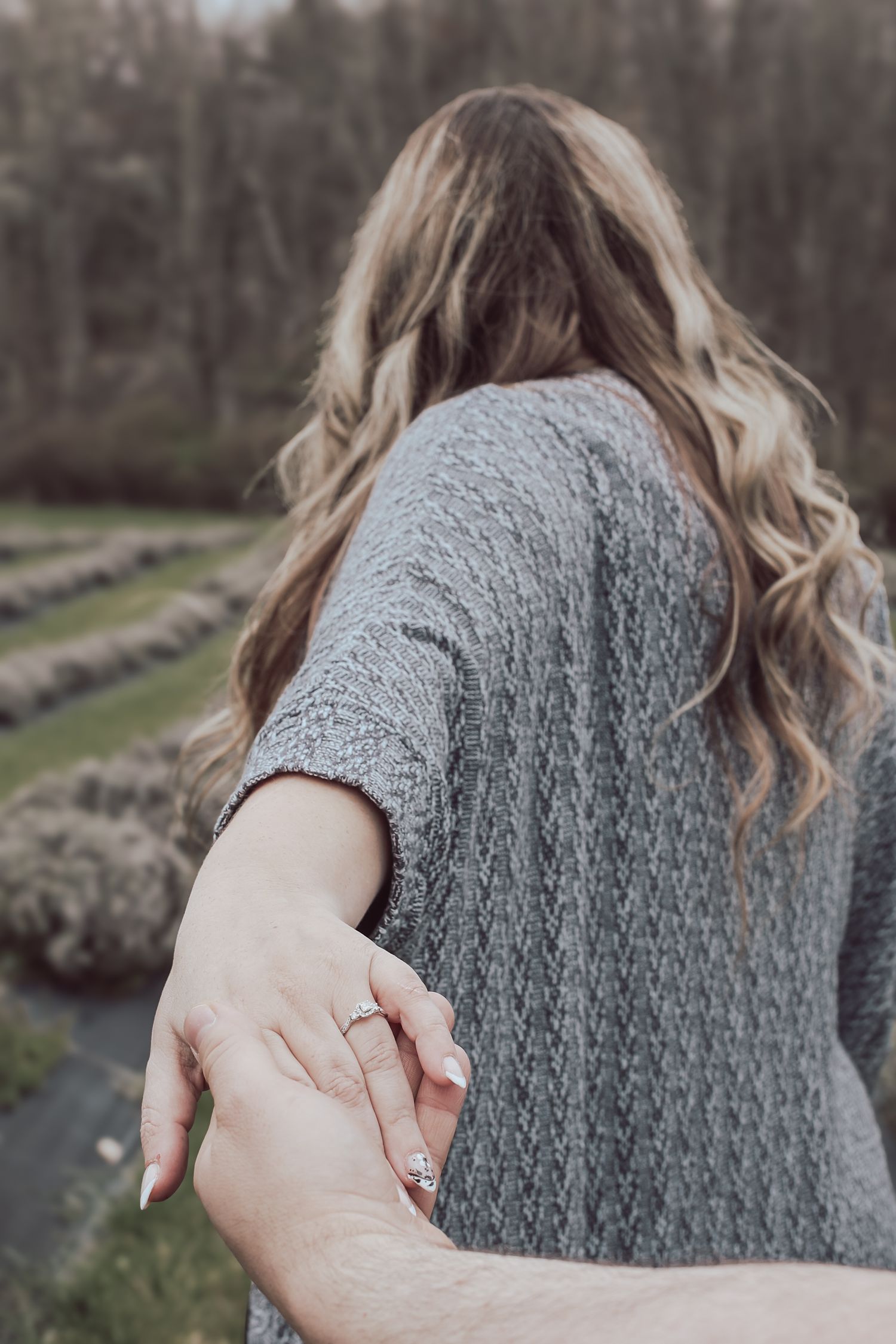 Back view of person wearing gray knitted sweater with textured pattern detail in outdoor setting.