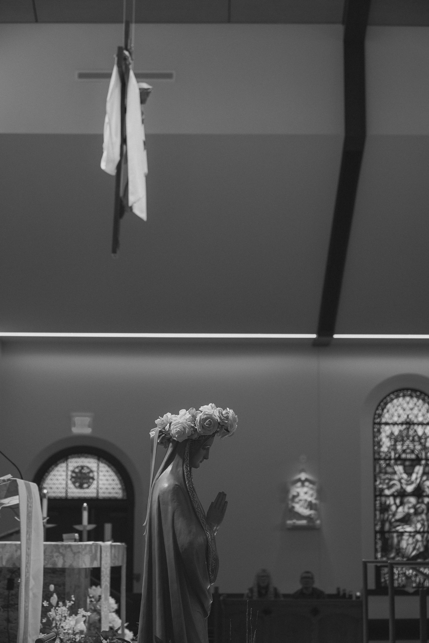A black and white interior of a church with stained glass windows and people gathering during a service.