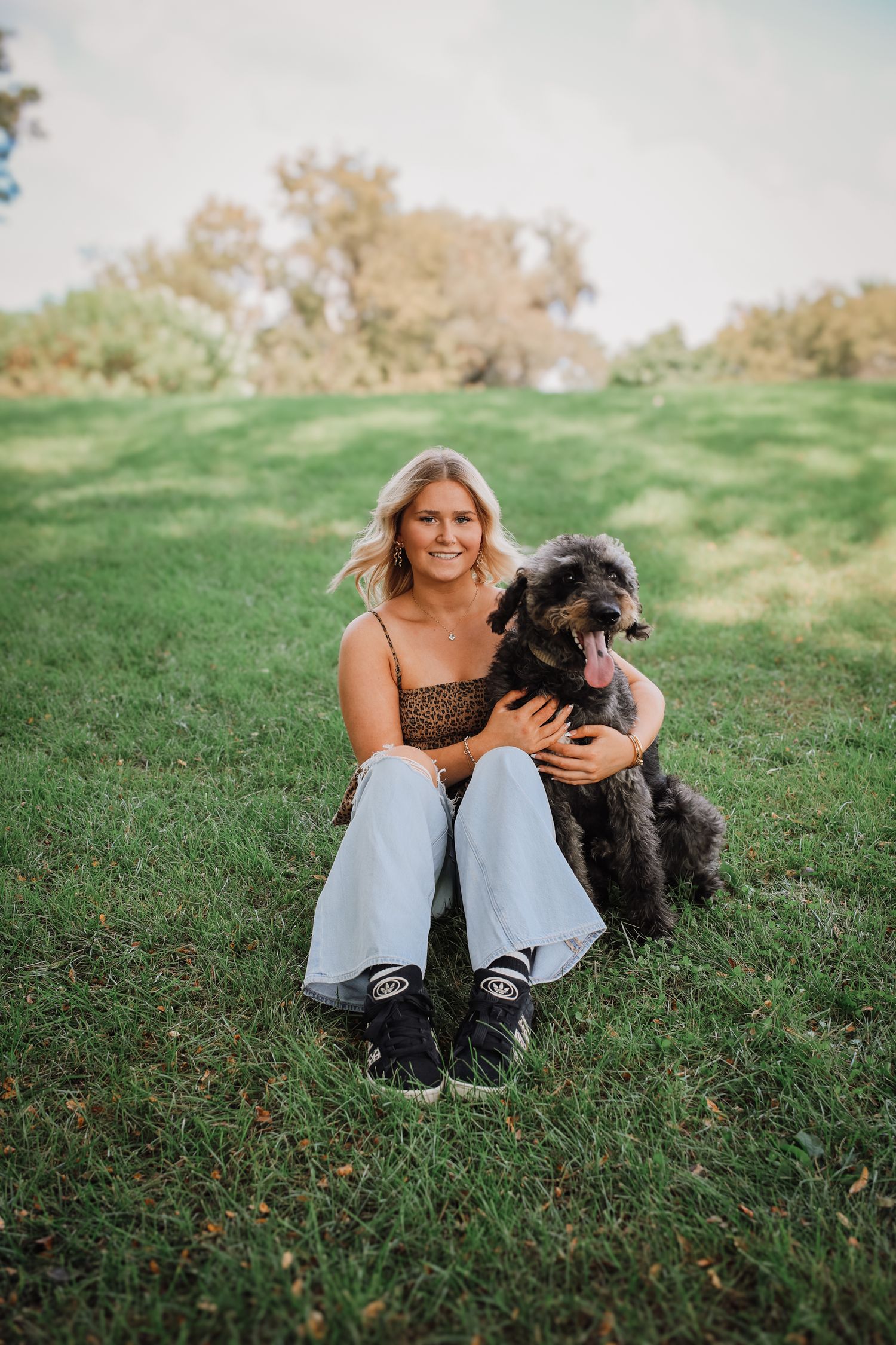 A person sits on green grass with a happy black shaggy dog on a sunny autumn day.