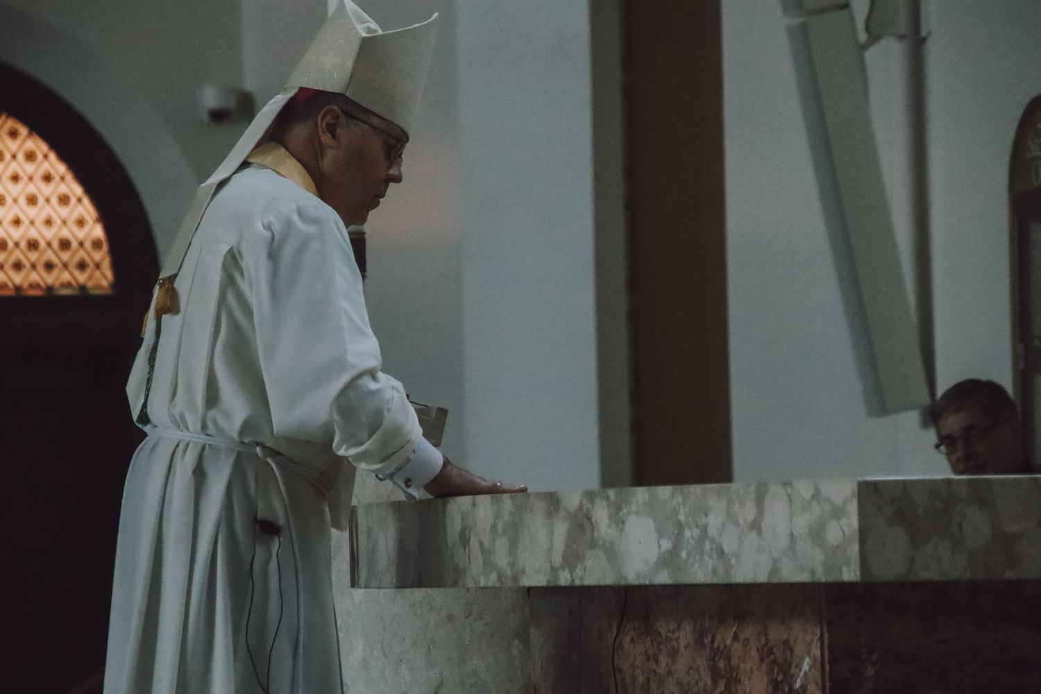A person wearing white religious robes stands at a marble altar inside a church during a ceremony.