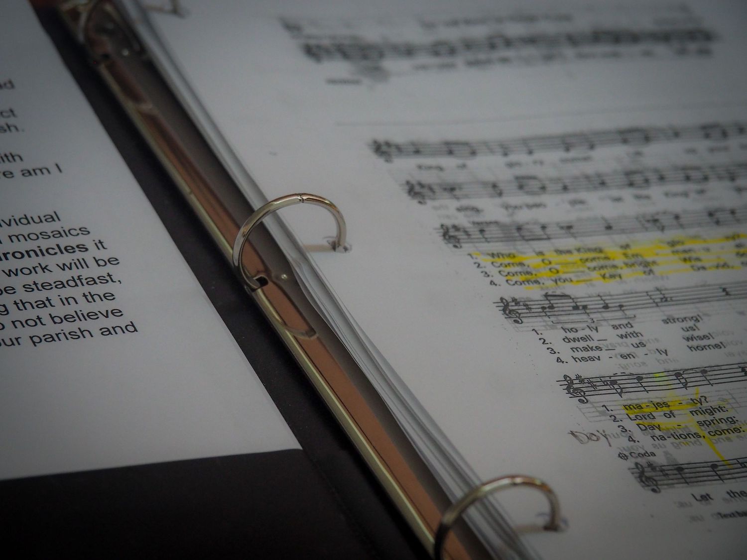 Sheet music in a binder with highlighted sections and metal rings visible in close-up view.