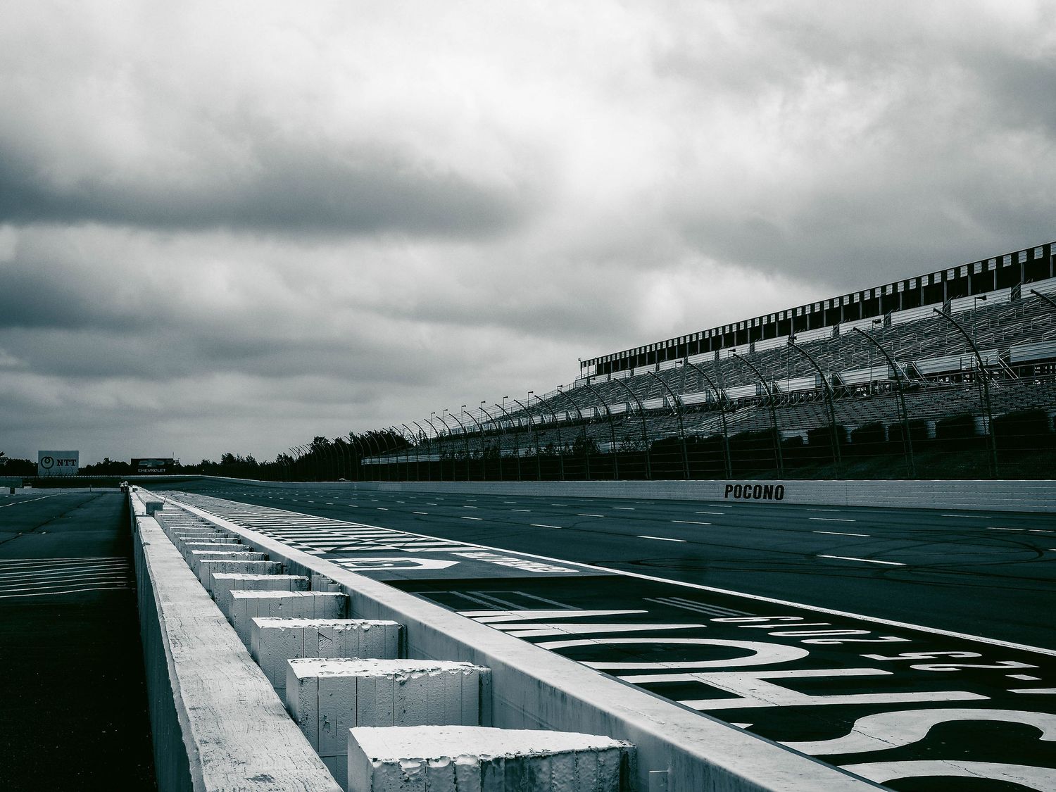 Empty race track stretches into the distance under dramatic cloudy skies at Pocono Raceway.