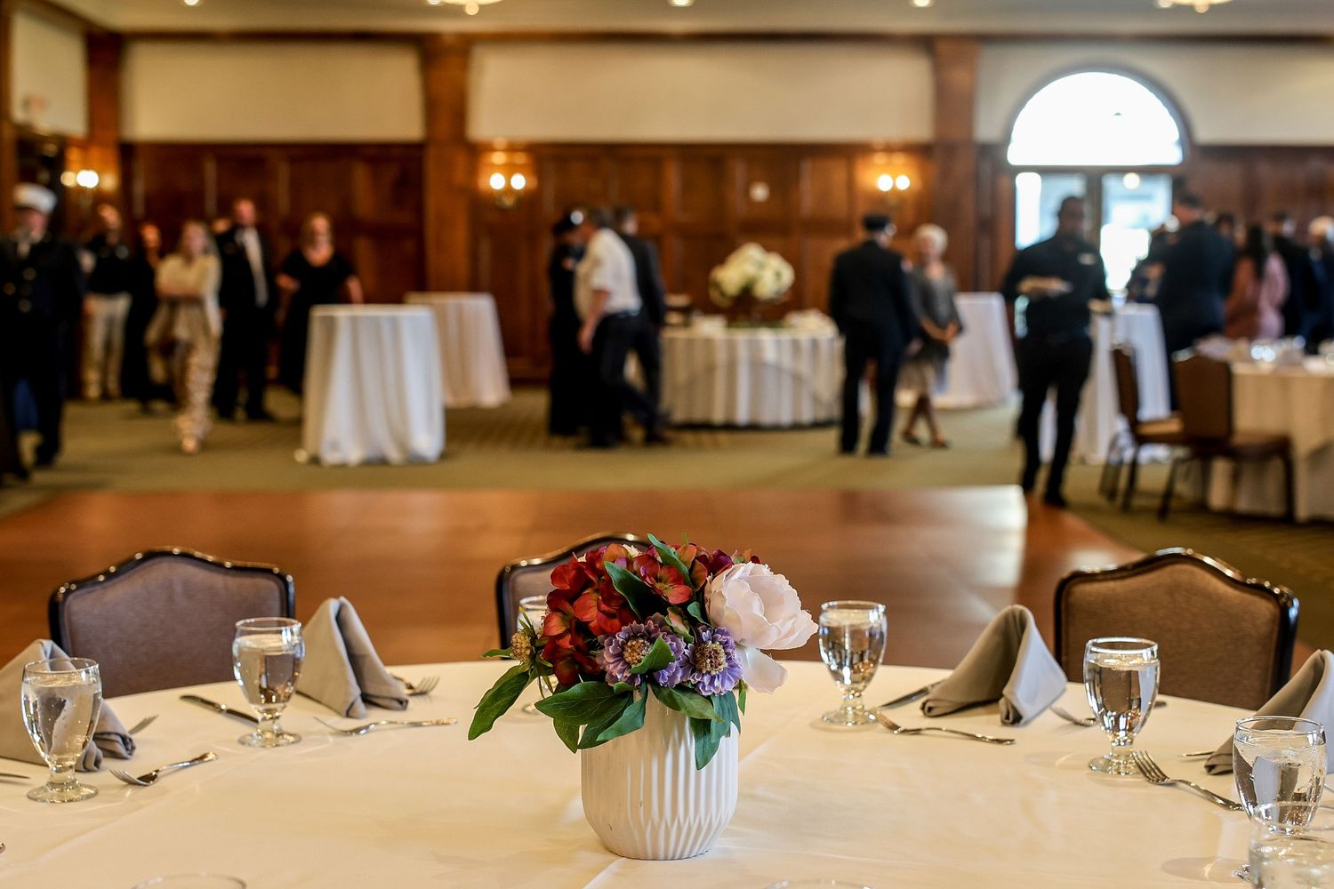 An elegant wedding reception venue with round tables, floral centerpieces, and warm lighting in a spacious ballroom.