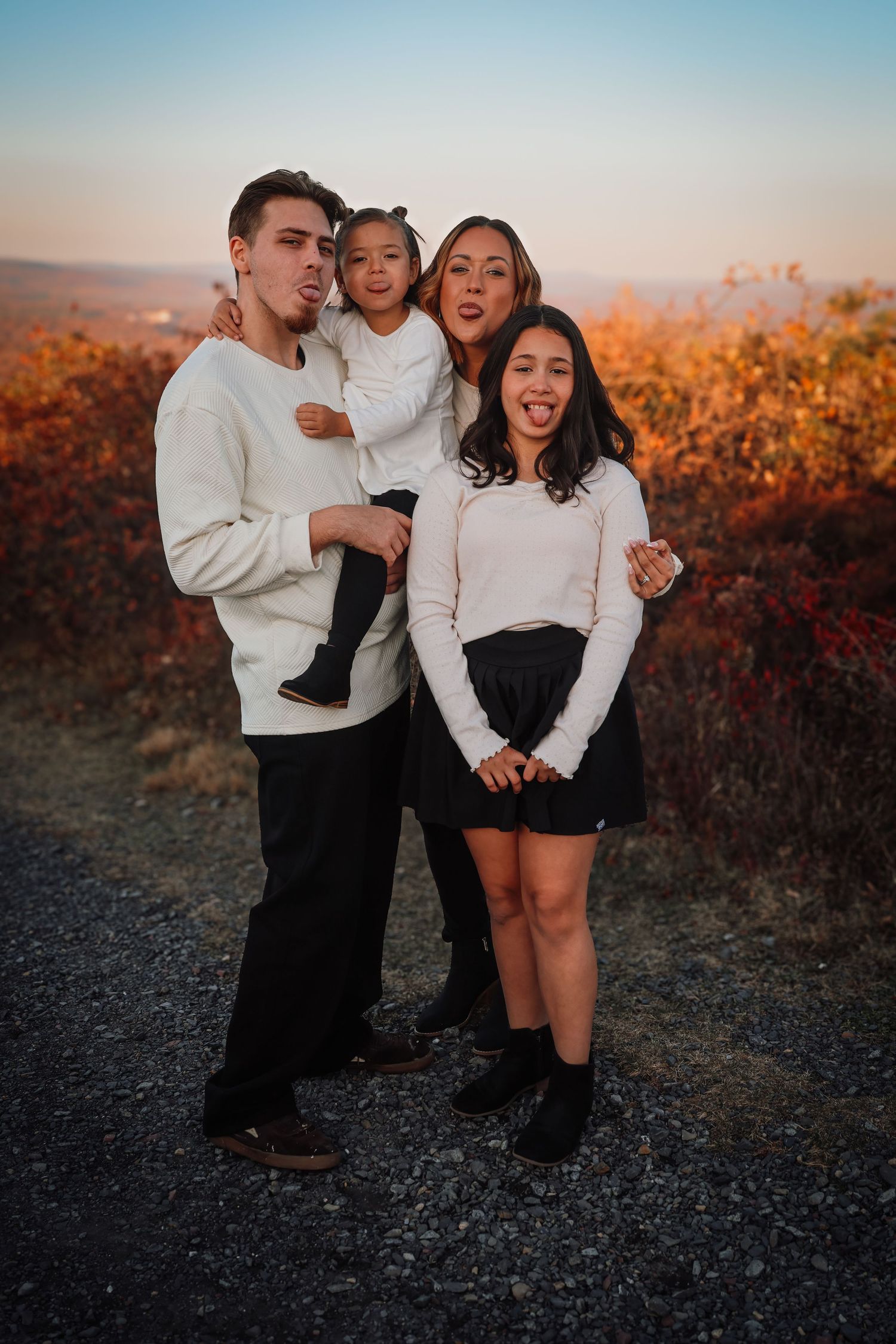 A family poses together for a portrait at sunset with autumn foliage in the background.