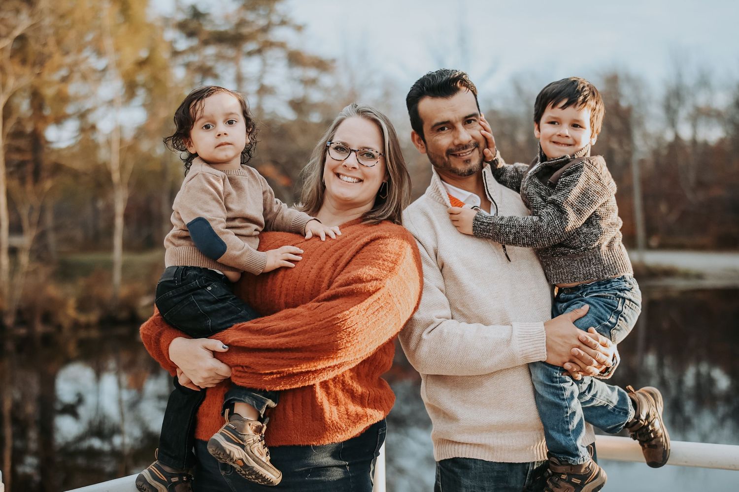 A group enjoys a playful autumn photo session outdoors by a lake with warm orange and neutral tones.