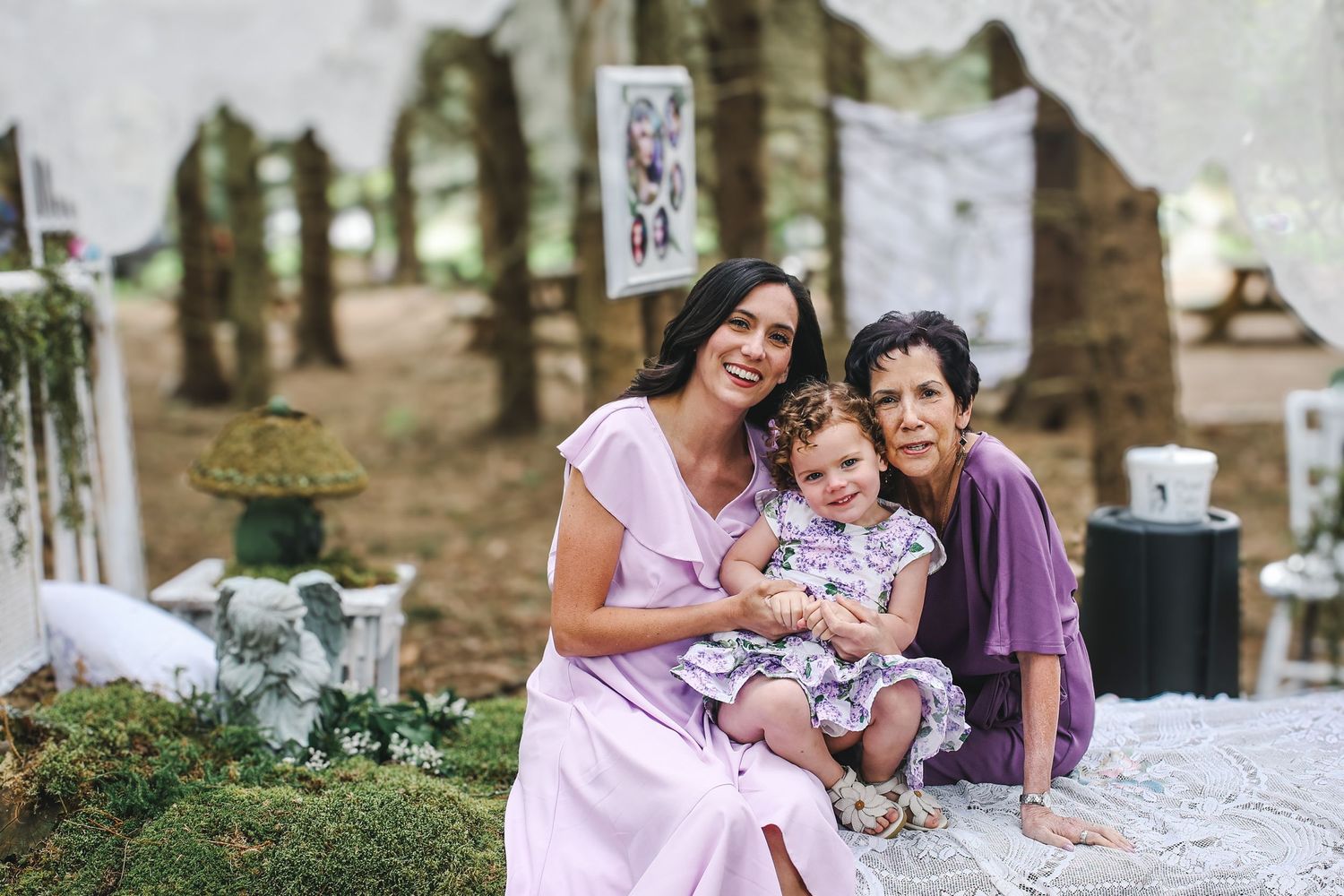 Family members sit together on a white blanket during an outdoor photo session in a park setting.