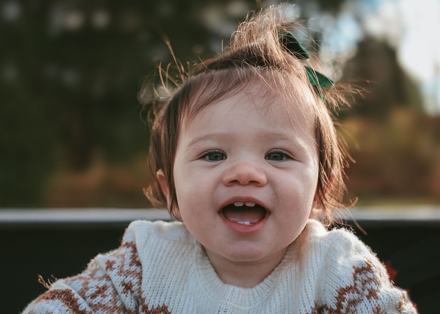 Happy baby wearing white collar sweater smiling outdoors.