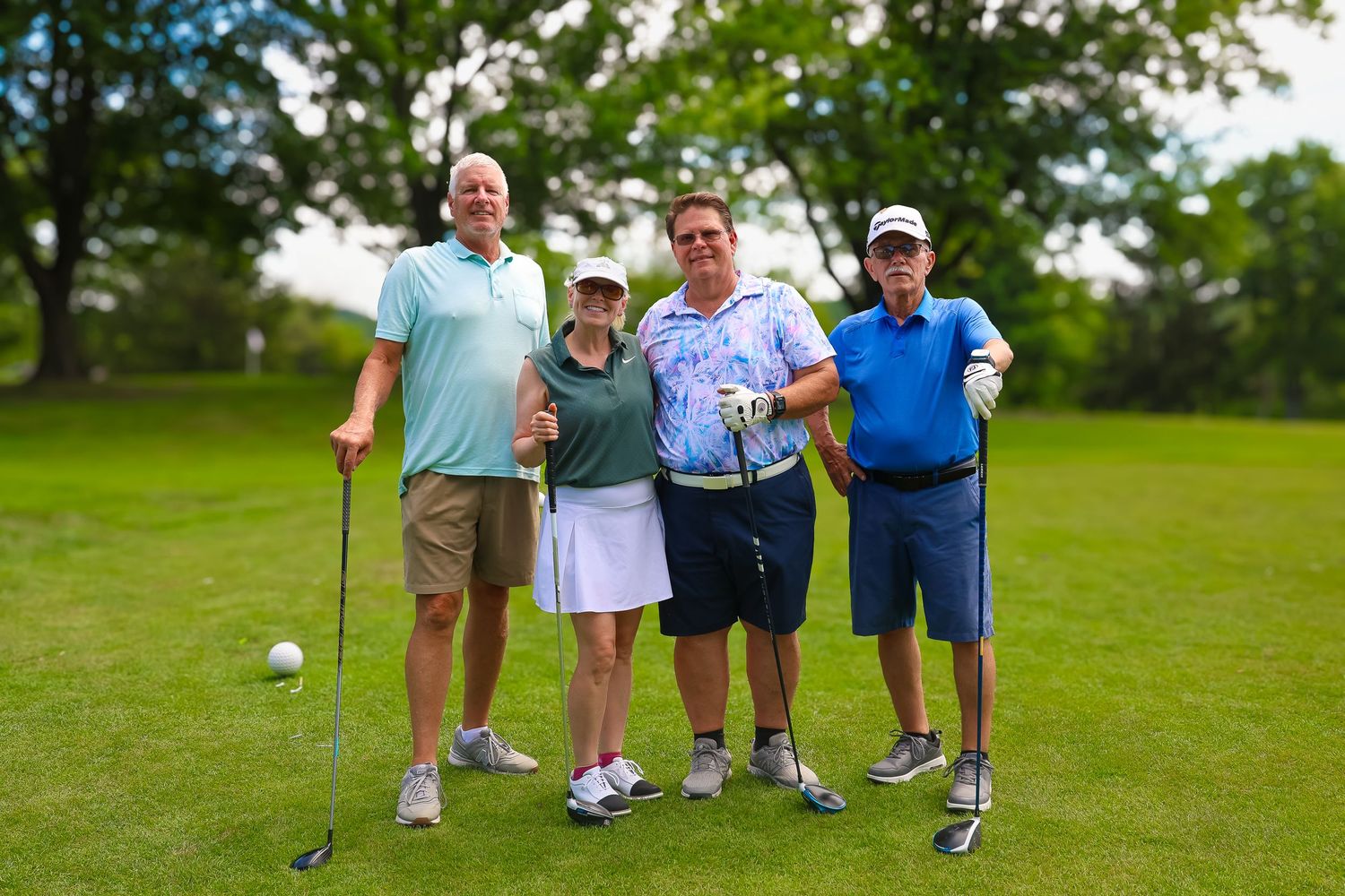 Four golfers standing together on a lush green golf course with clubs and smiling at the camera.
