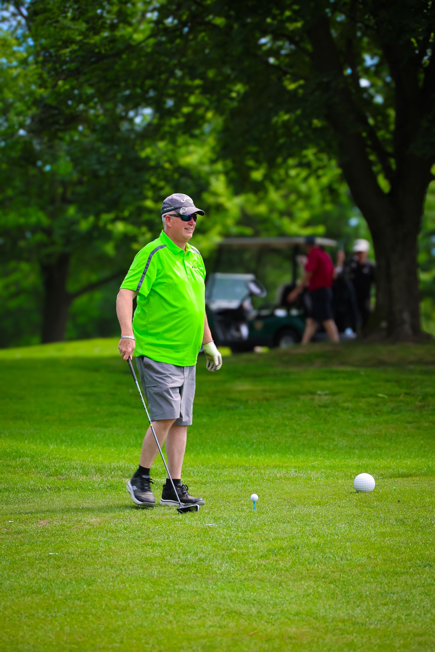 A golfer in a bright neon green shirt lines up a putt on a lush green course during a summer day.