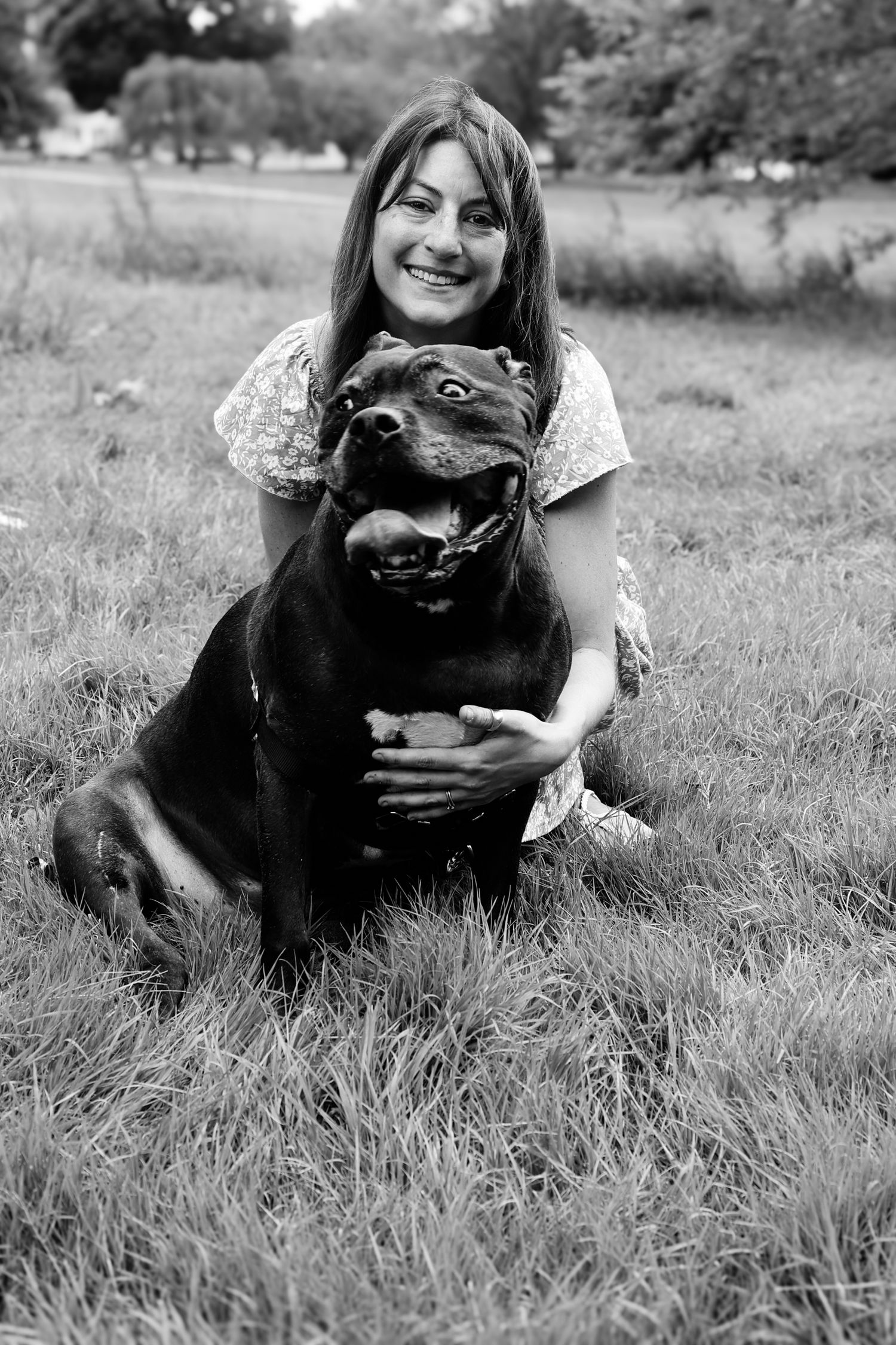 Black and white photos show someone lying in grass embracing a happy black Labrador retriever dog.