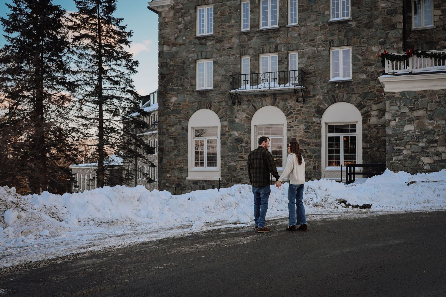 A stone building exterior with multiple windows is surrounded by snowy winter landscape at dusk.