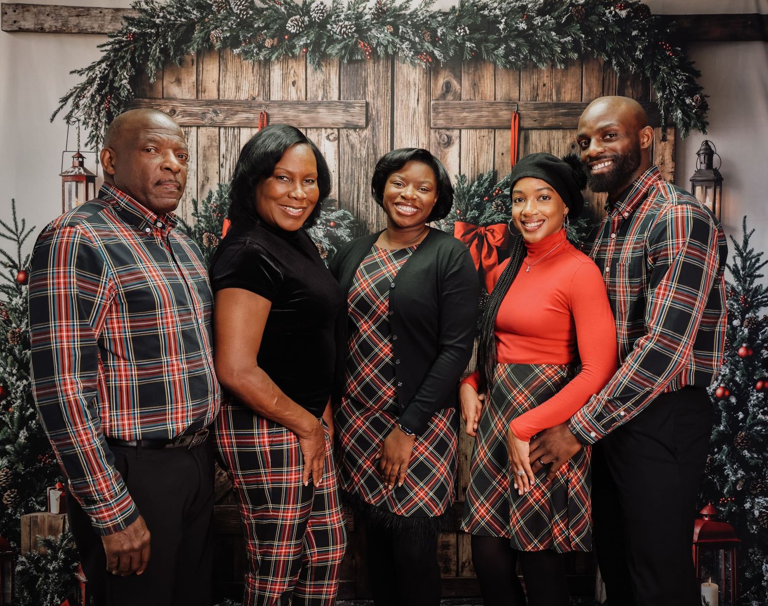 Family portrait session with coordinating red and black plaid outfits against a holiday-themed backdrop.