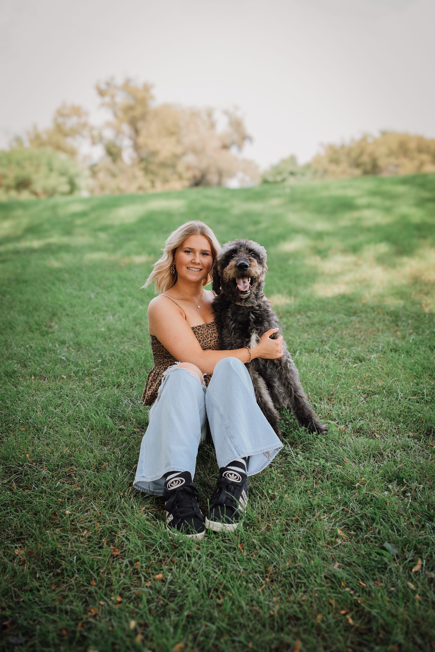 A series of photos showing a person and their black dog relaxing together on a grassy hillside.