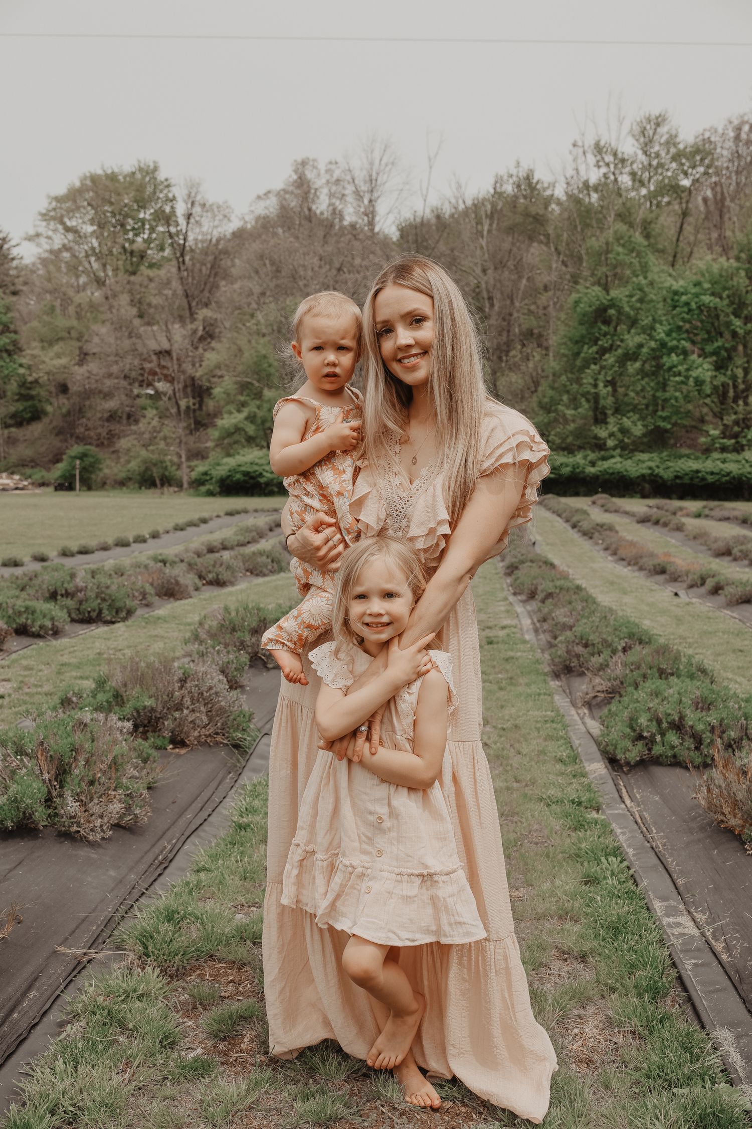 Family wearing matching peach dresses poses together in a garden with rows of lavender plants on a spring day.