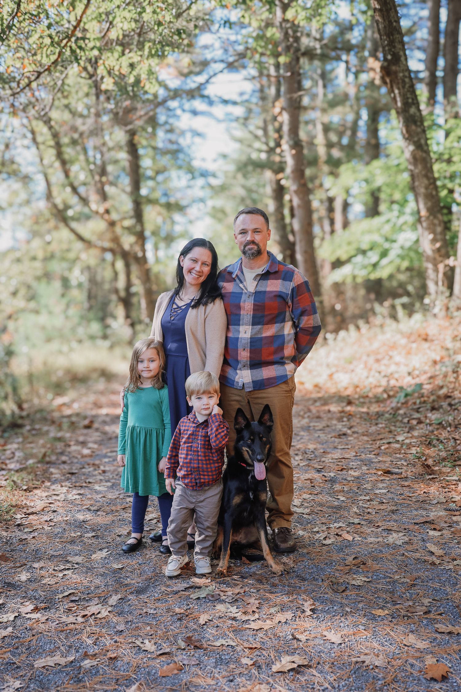 Family poses together on a leaf-covered forest trail during an autumn photoshoot.