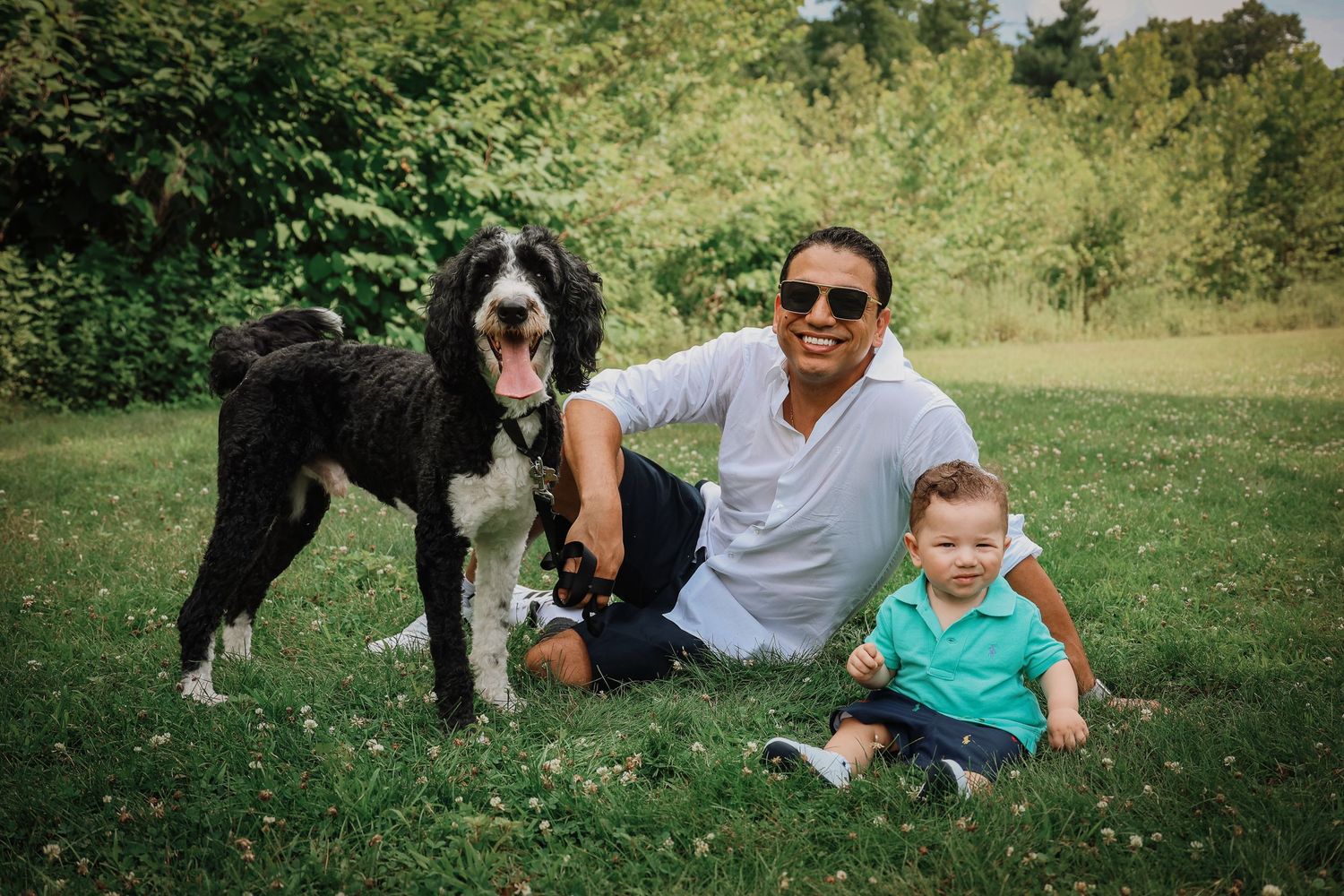 A family relaxes together on green grass during a sunny outdoor photoshoot session.