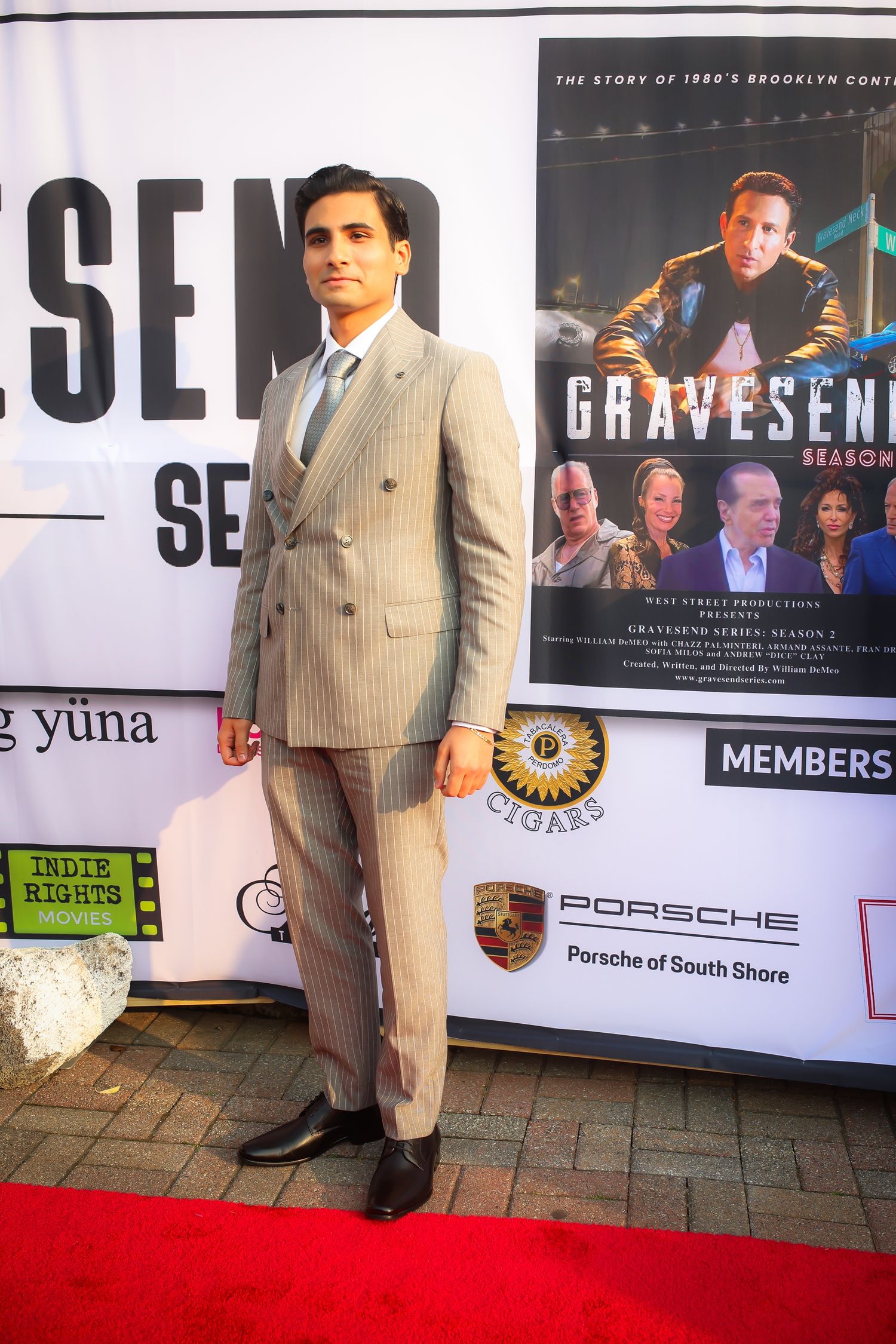 A person wearing a light colored pinstripe suit stands in front of promotional signage and posters at an event.