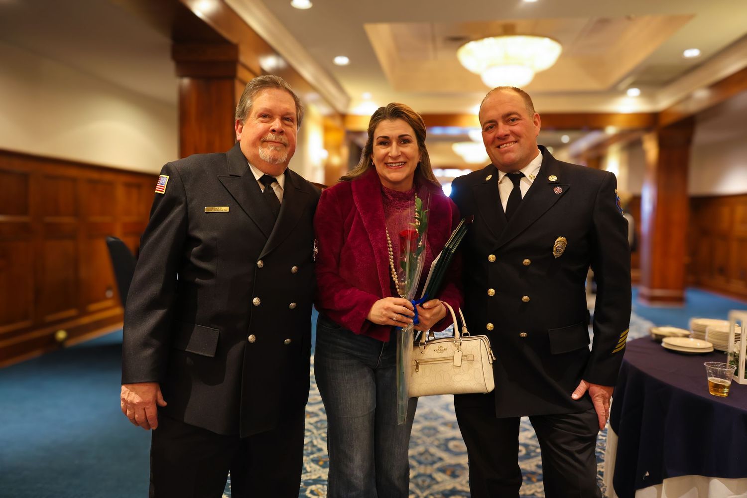 Group of uniformed officers and civilians gathered in an elegant wood-paneled hallway with warm lighting.