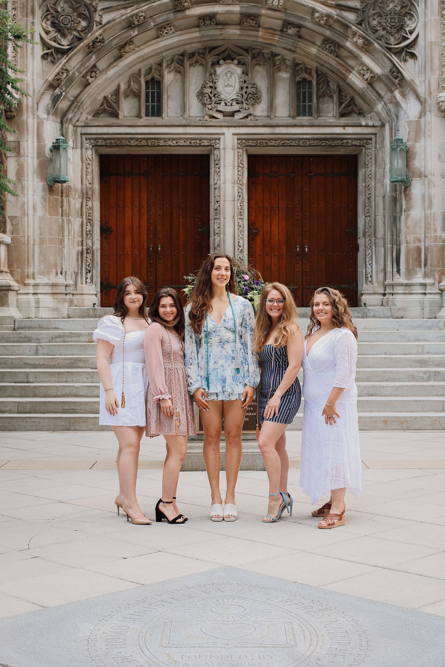 A group stands together on stone steps in front of ornate gothic architecture wearing light summer outfits.