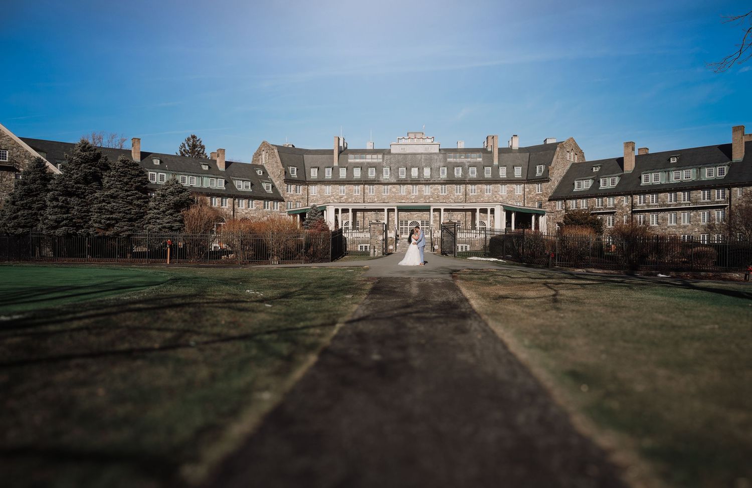 Panoramic view of a historic stone mansion with manicured grounds and dramatic shadows cast across the lawn.