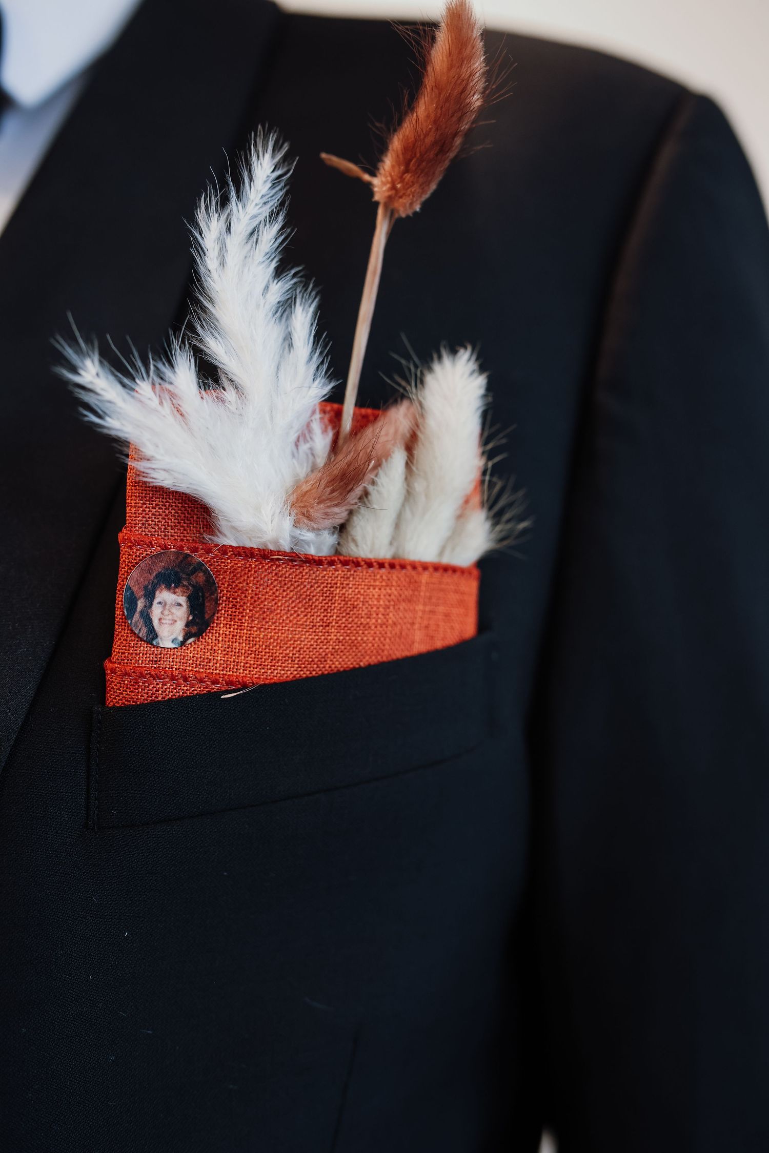 Close-up sequence showing white feathers and orange fabric decorative elements arranged in a pocket square against a dark suit.