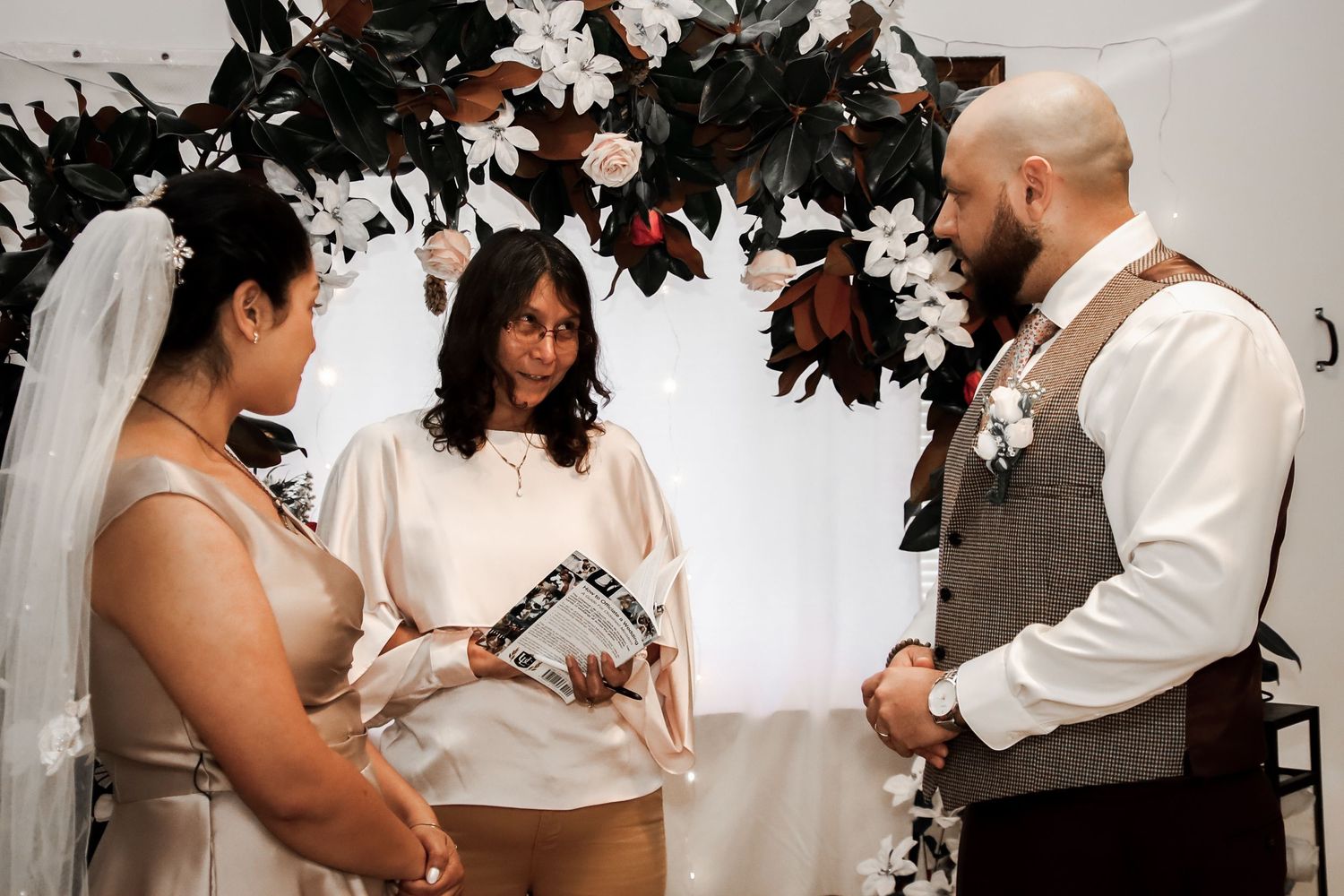 A couple shares an intimate moment during their wedding ceremony with white decor and floral elements in the background.