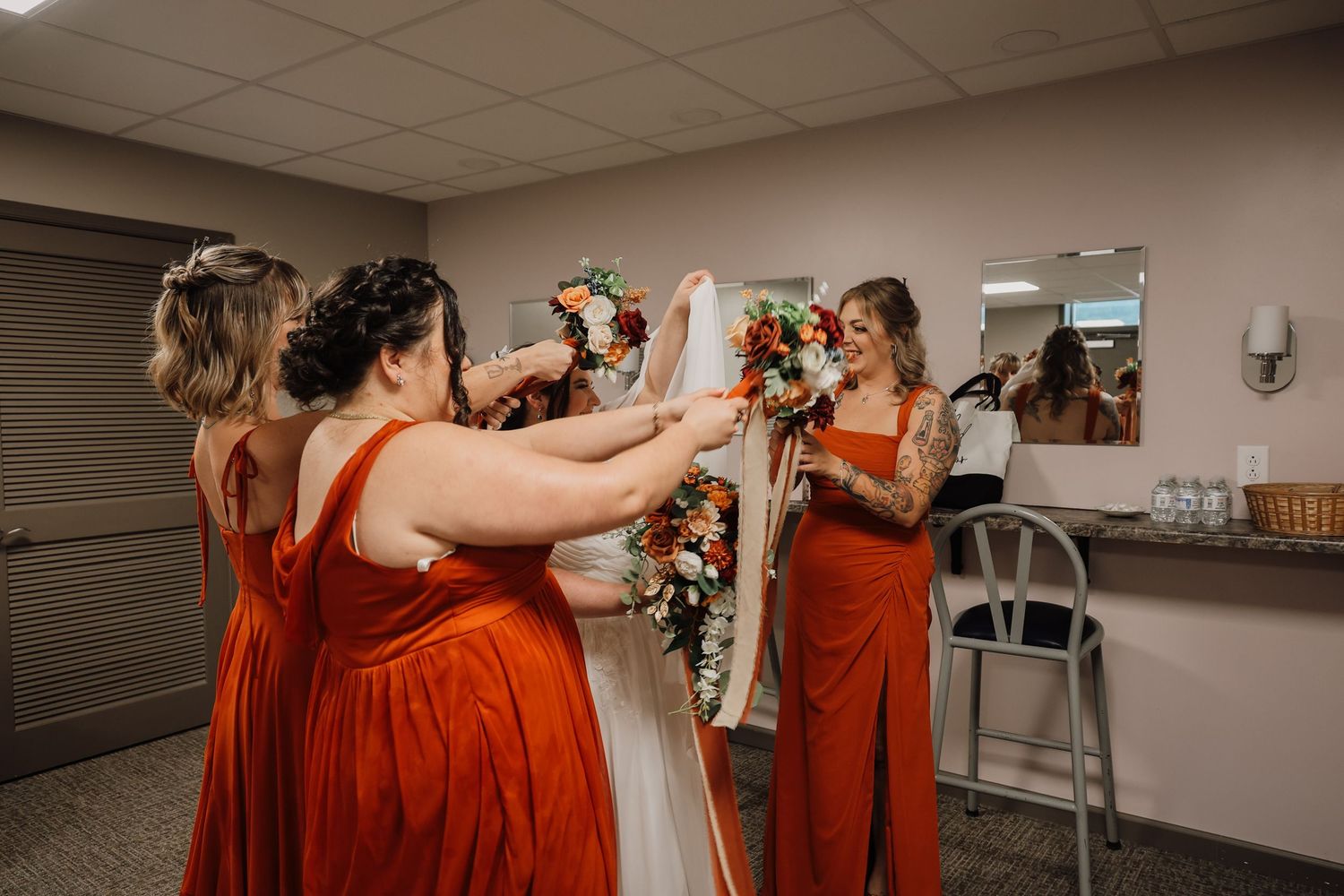 A group of bridesmaids in rust-colored dresses share an emotional moment during a wedding celebration.