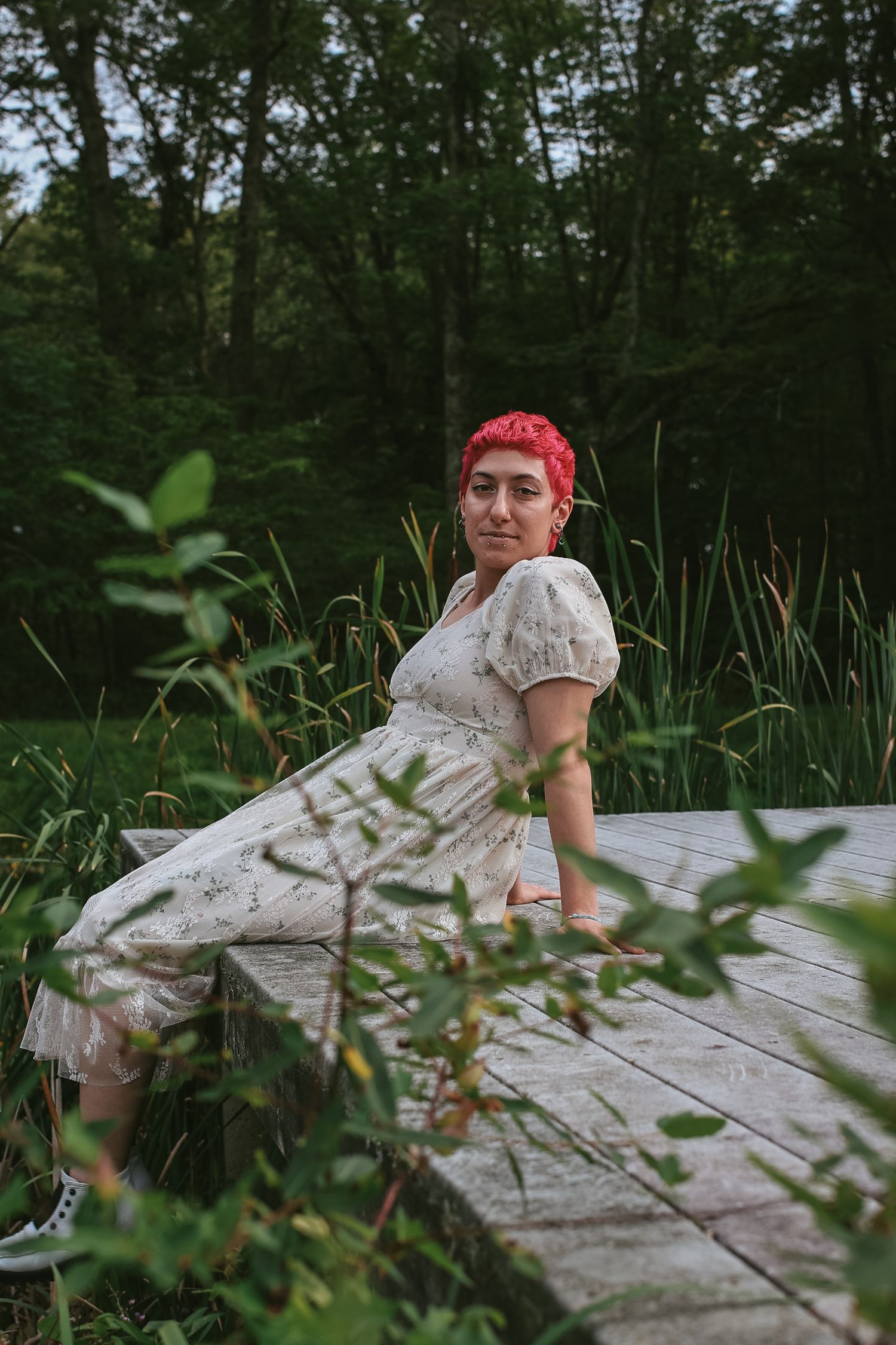 Person in red bandana relaxes on a fallen log surrounded by lush green forest vegetation.