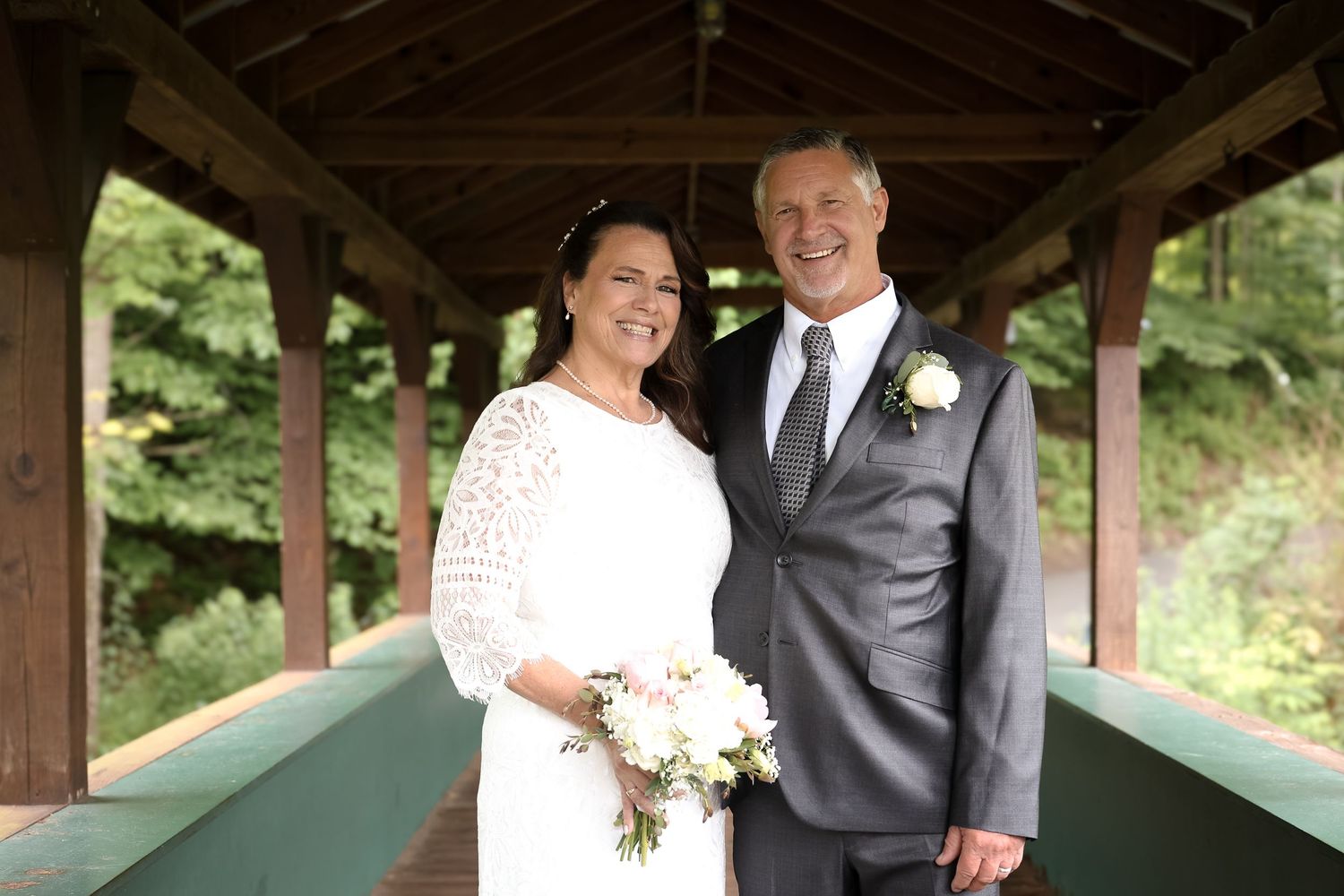A happy couple shares a romantic moment under a covered wooden bridge during their wedding day celebration.