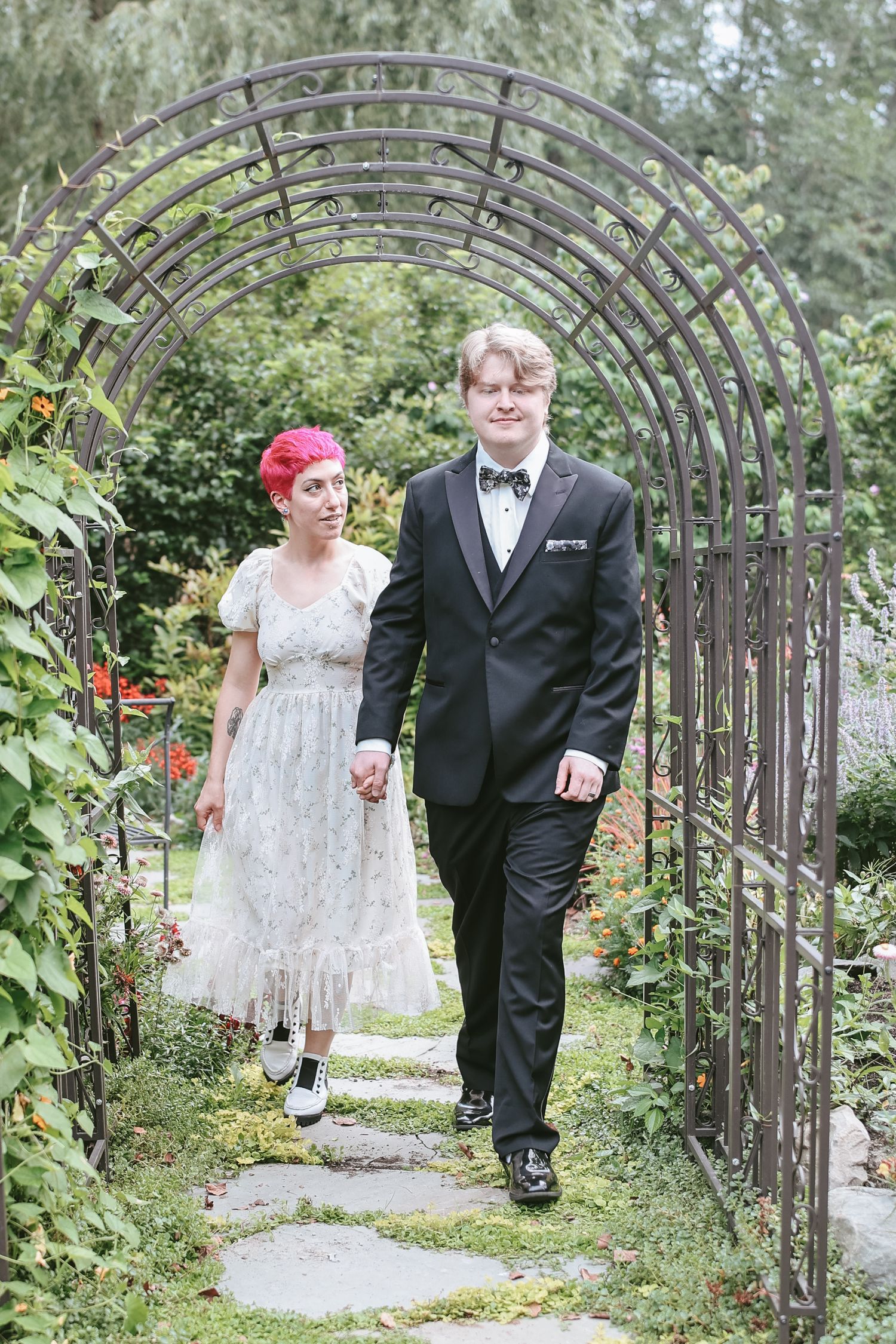 A couple walks together through a rustic garden archway on their wedding day.