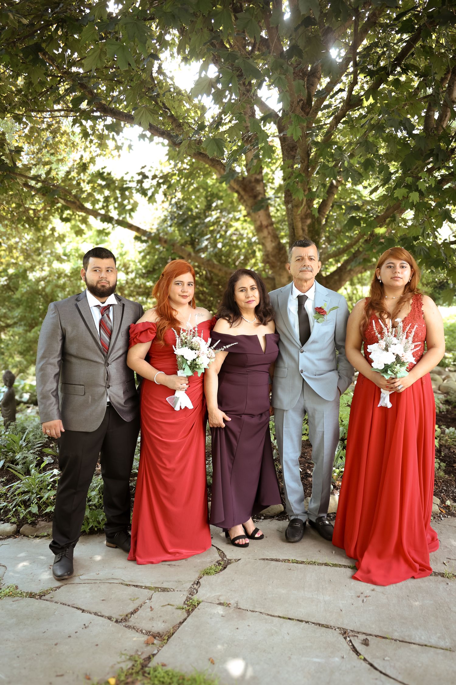 Wedding party poses together in garden setting wearing red and purple dresses with gray suits.