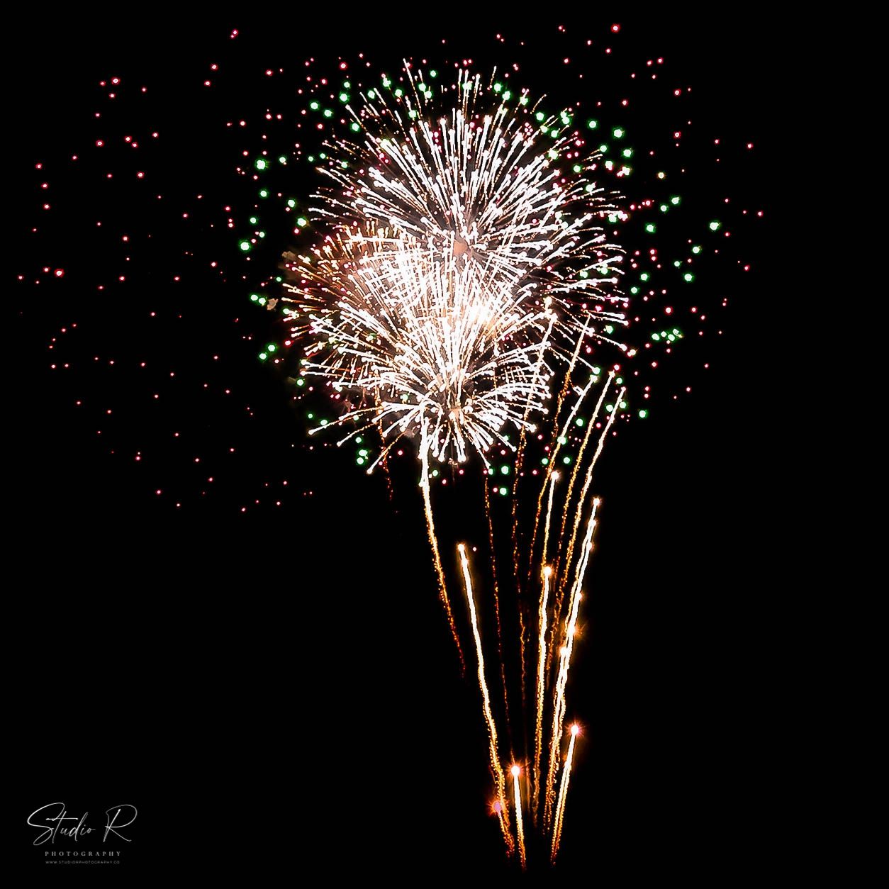 Colorful fireworks bursting in a dark night sky with white, green, and red sparks, captured in a square photo.
