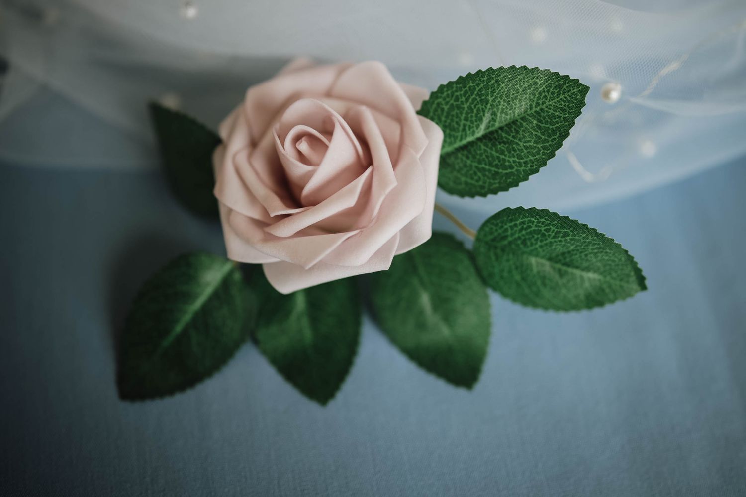 Close-up of a delicate pink artificial rose with green leaves as a wedding decoration.