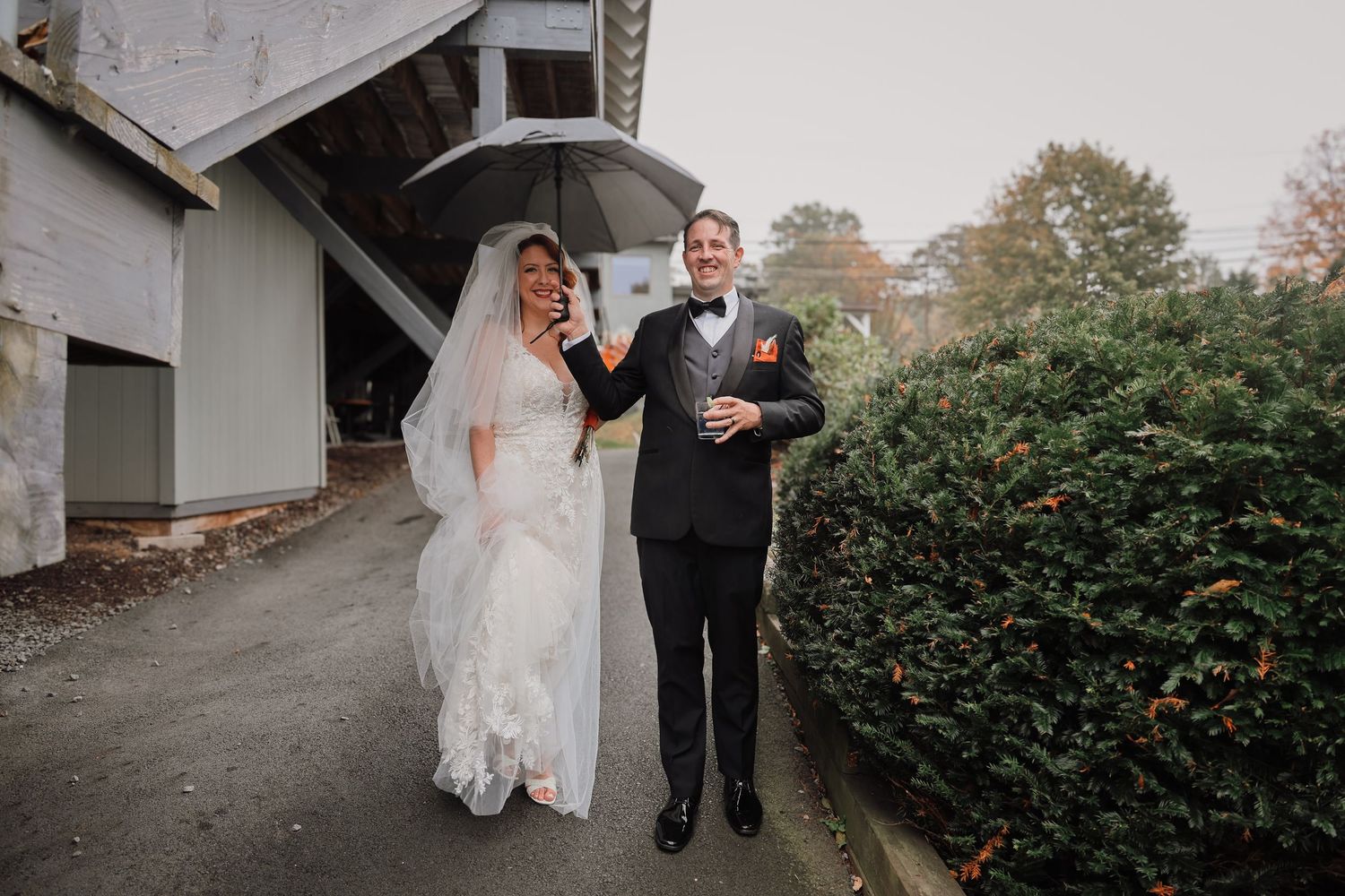 A couple shares an umbrella while walking together on their rainy wedding day outside a stone building.