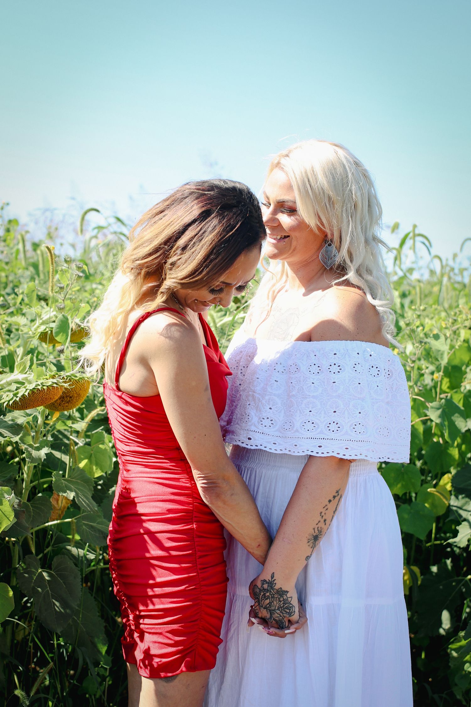 Couple in red and white dresses standing together in a sunny vineyard.