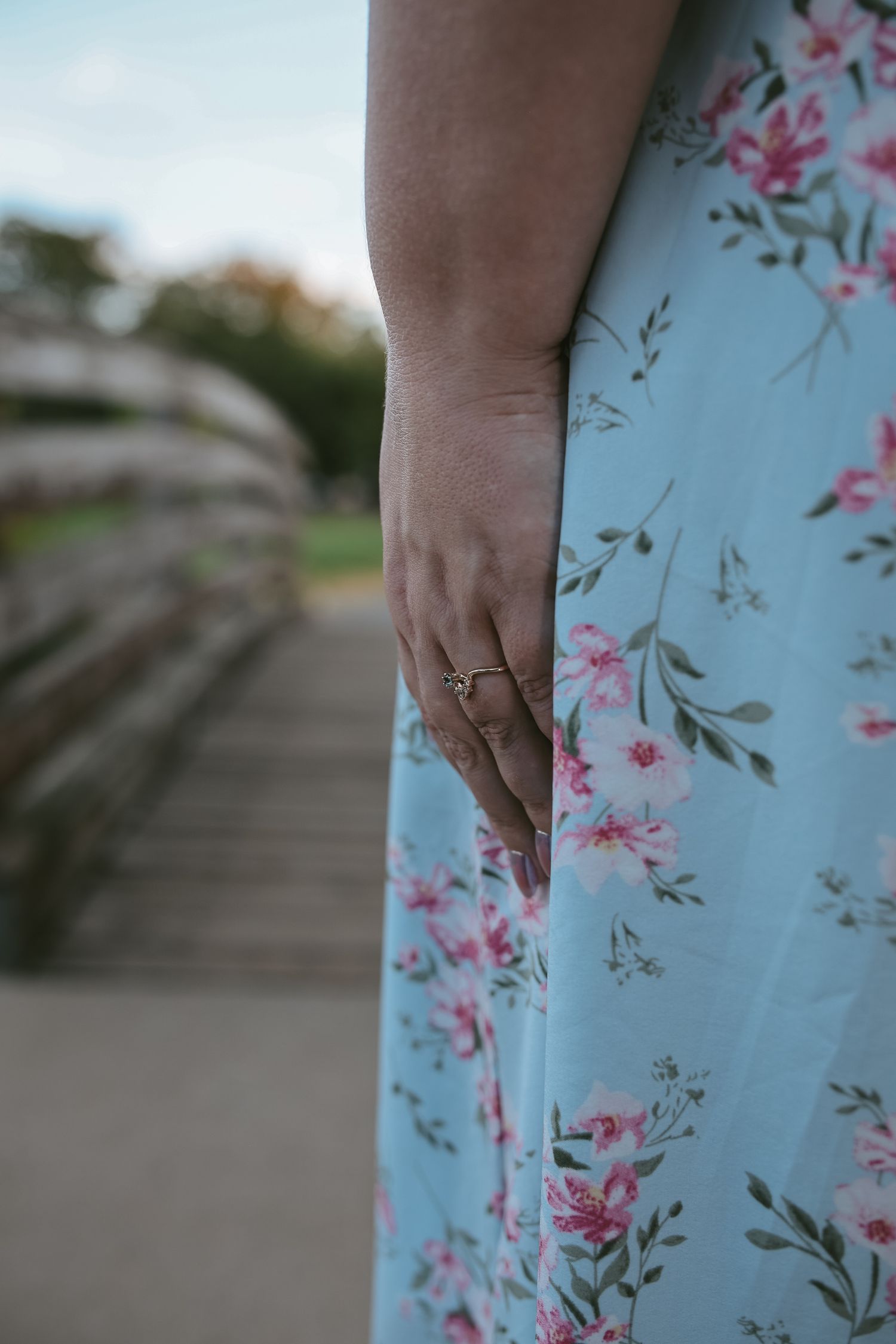 Close-up view of a floral dress fabric with pink blossoms and green leaves on a light blue background.