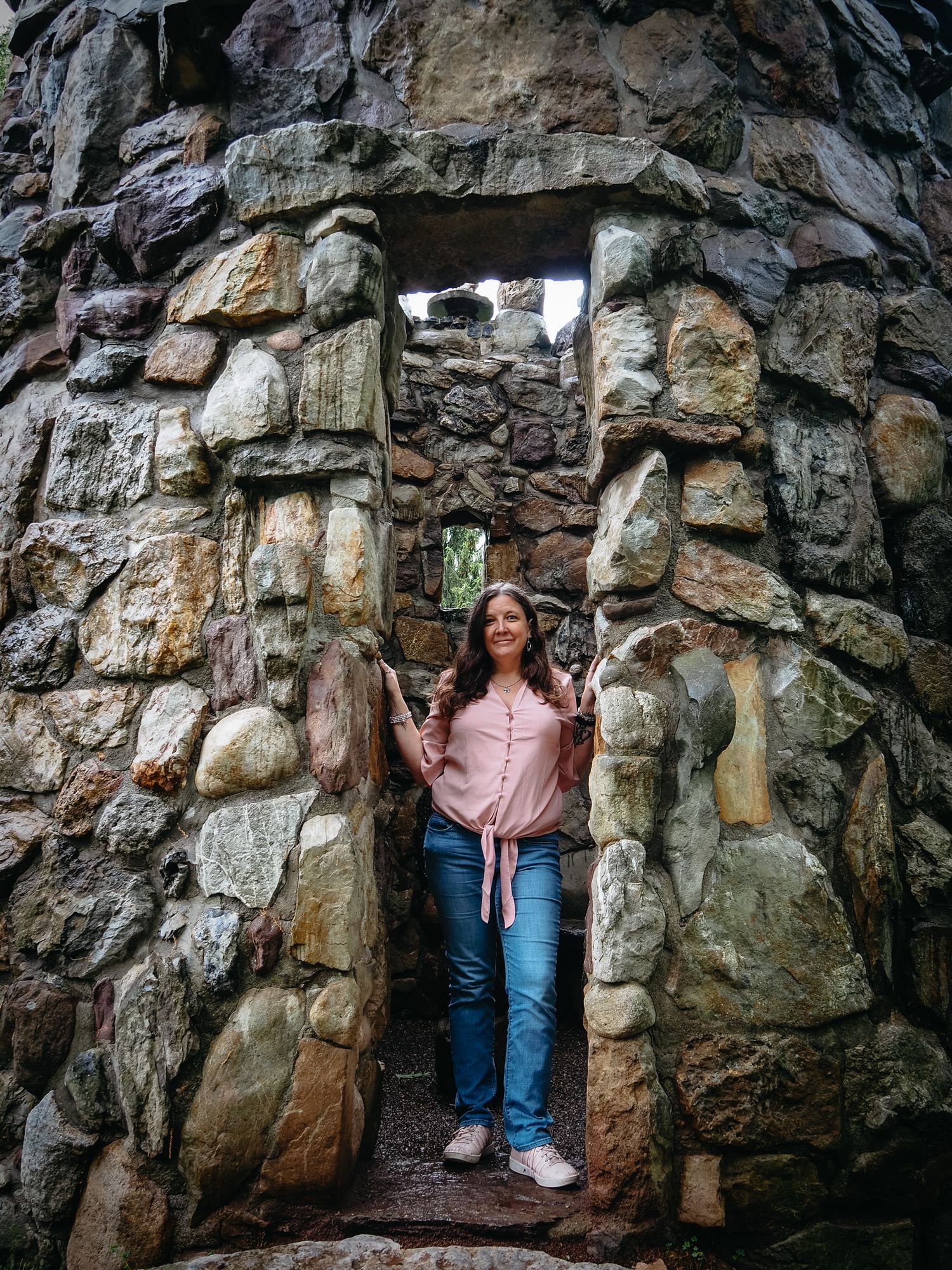 A series of four photos showing a person in jeans and pink top exploring a rocky cave wall formation.