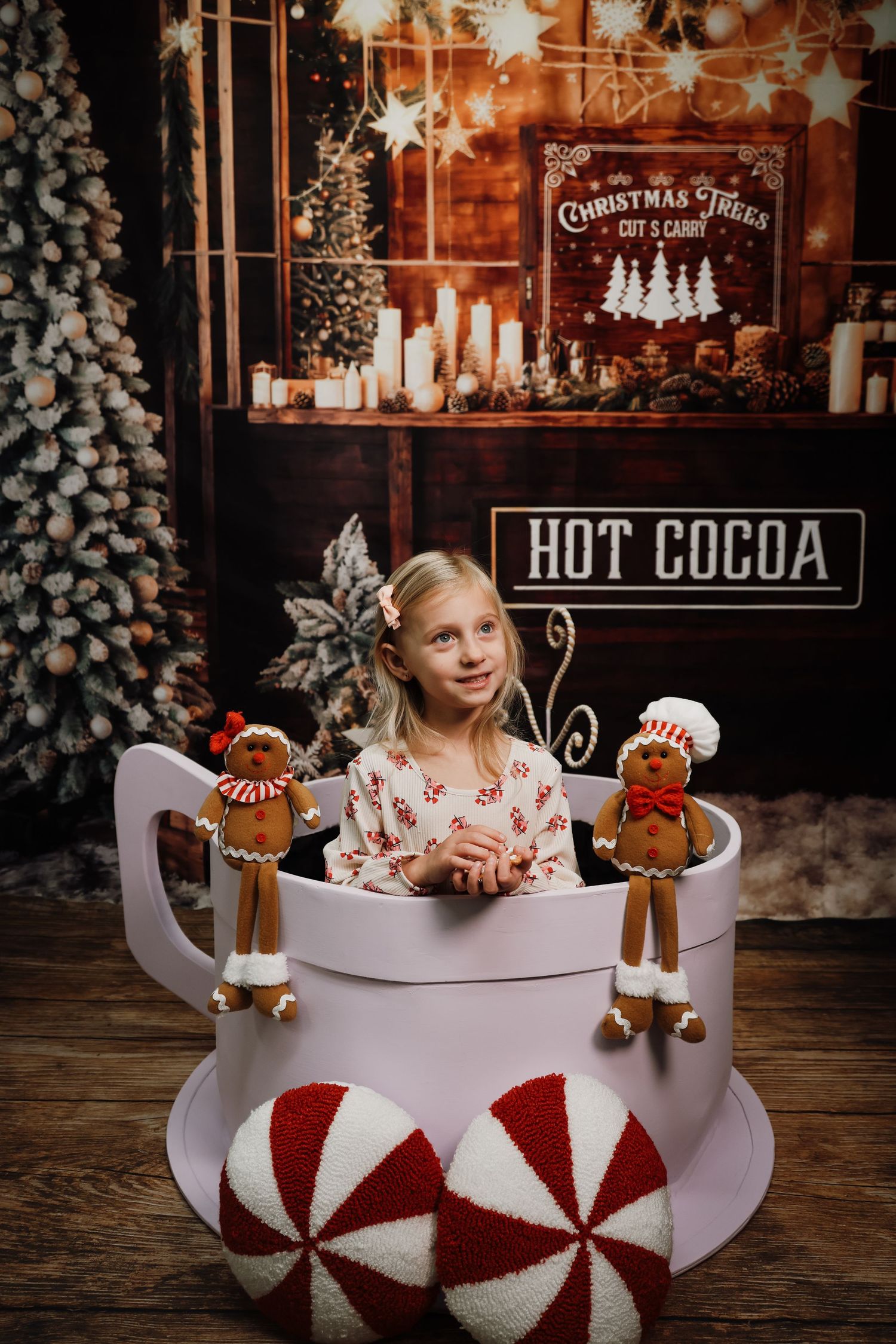 Festive Christmas scene with giant hot cocoa mug prop, gingerbread decorations and peppermint cushions in warm lighting.