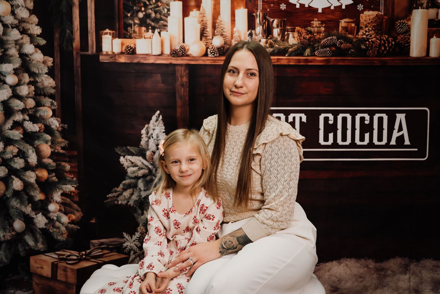 A cozy winter scene with two people sitting together in front of a hot cocoa sign and holiday decorations.