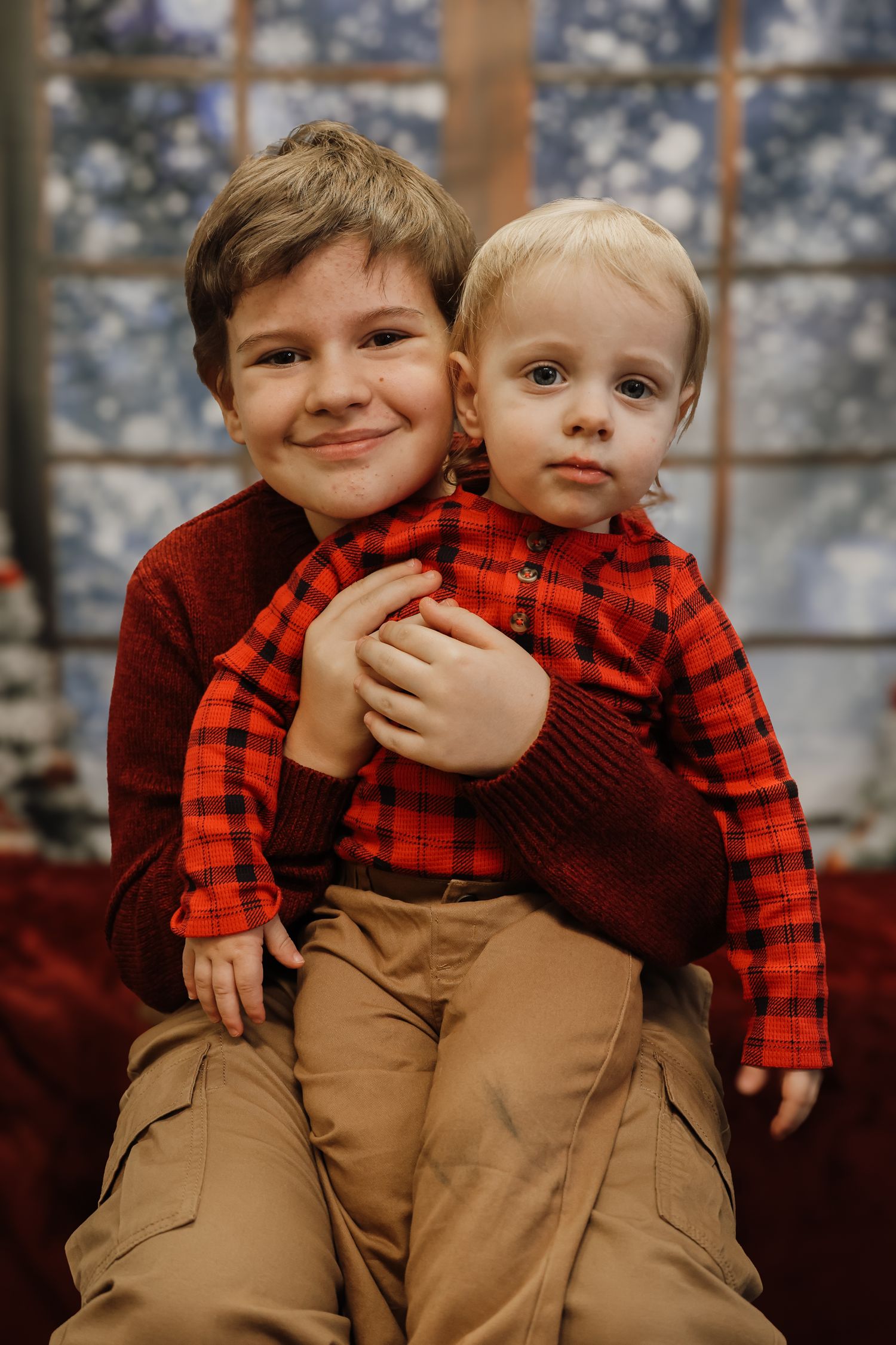 Two young children in red buffalo plaid and khaki overalls pose together in a series of candid holiday portraits.