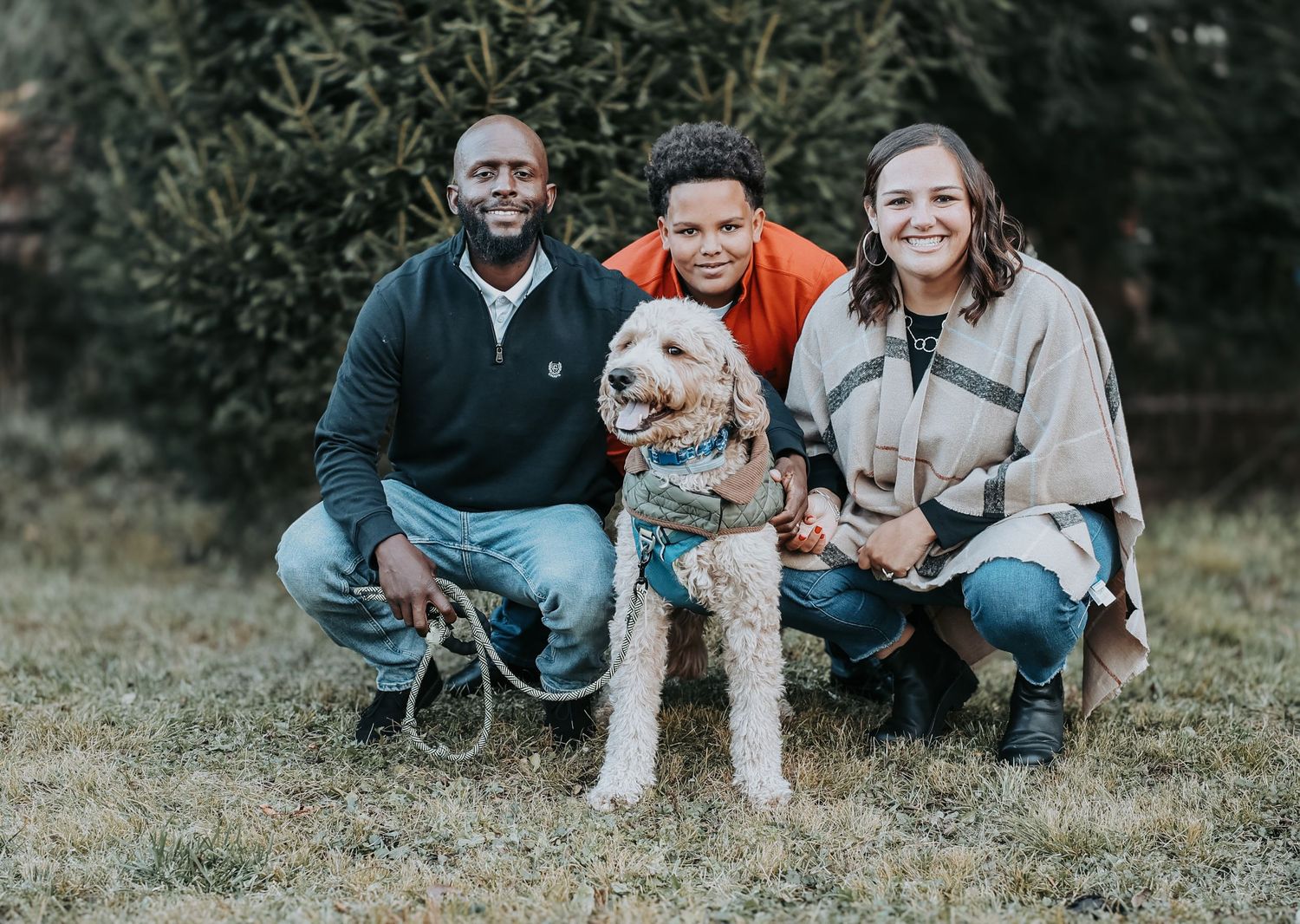 A group relaxes together outdoors on grass with their small dogs during an autumn photoshoot.
