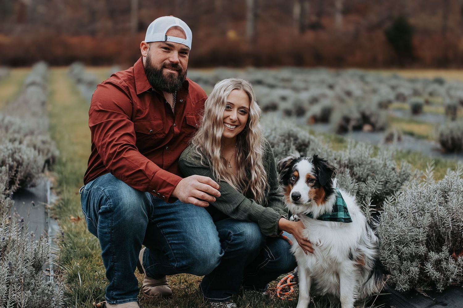 A couple sits in a field of sagebrush with their Australian Shepherd dog during an outdoor photo session.