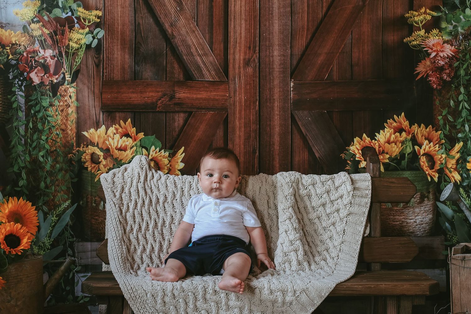 A white wicker chair with floral decorations and rustic wooden barn doors creates a charming autumn photo setting.