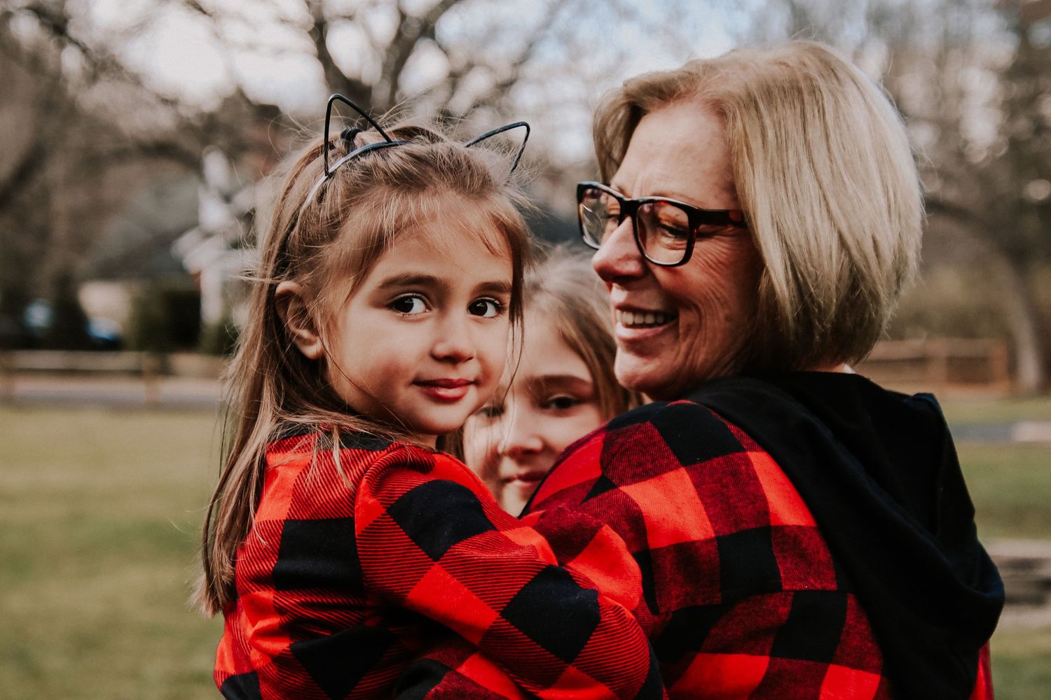 A family wearing matching red and black buffalo plaid outfits embraces while taking photos outdoors in winter.