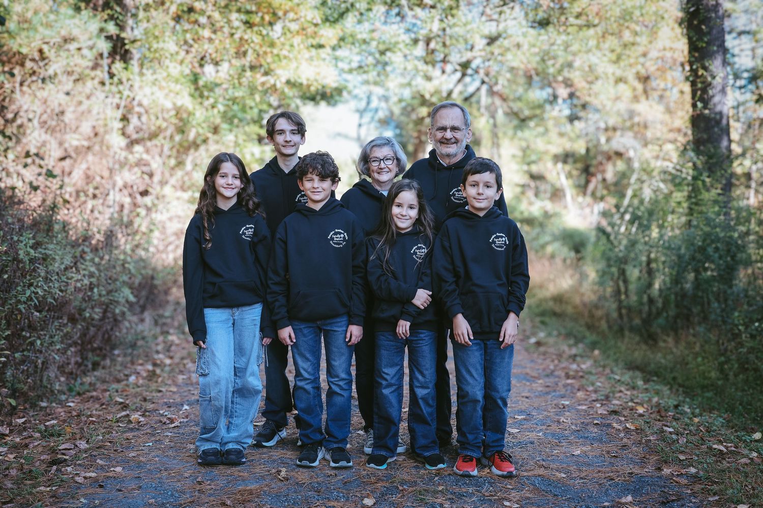 A family group poses together on a wooded trail while wearing coordinated black sweatshirts.