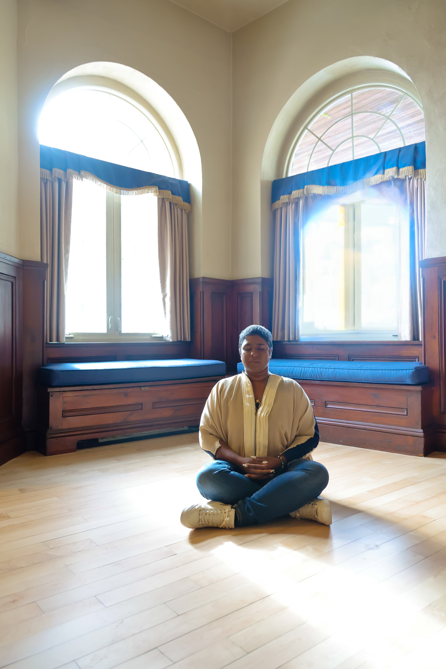 A series of yoga meditation poses shown in an empty room with wooden floors and arched windows.