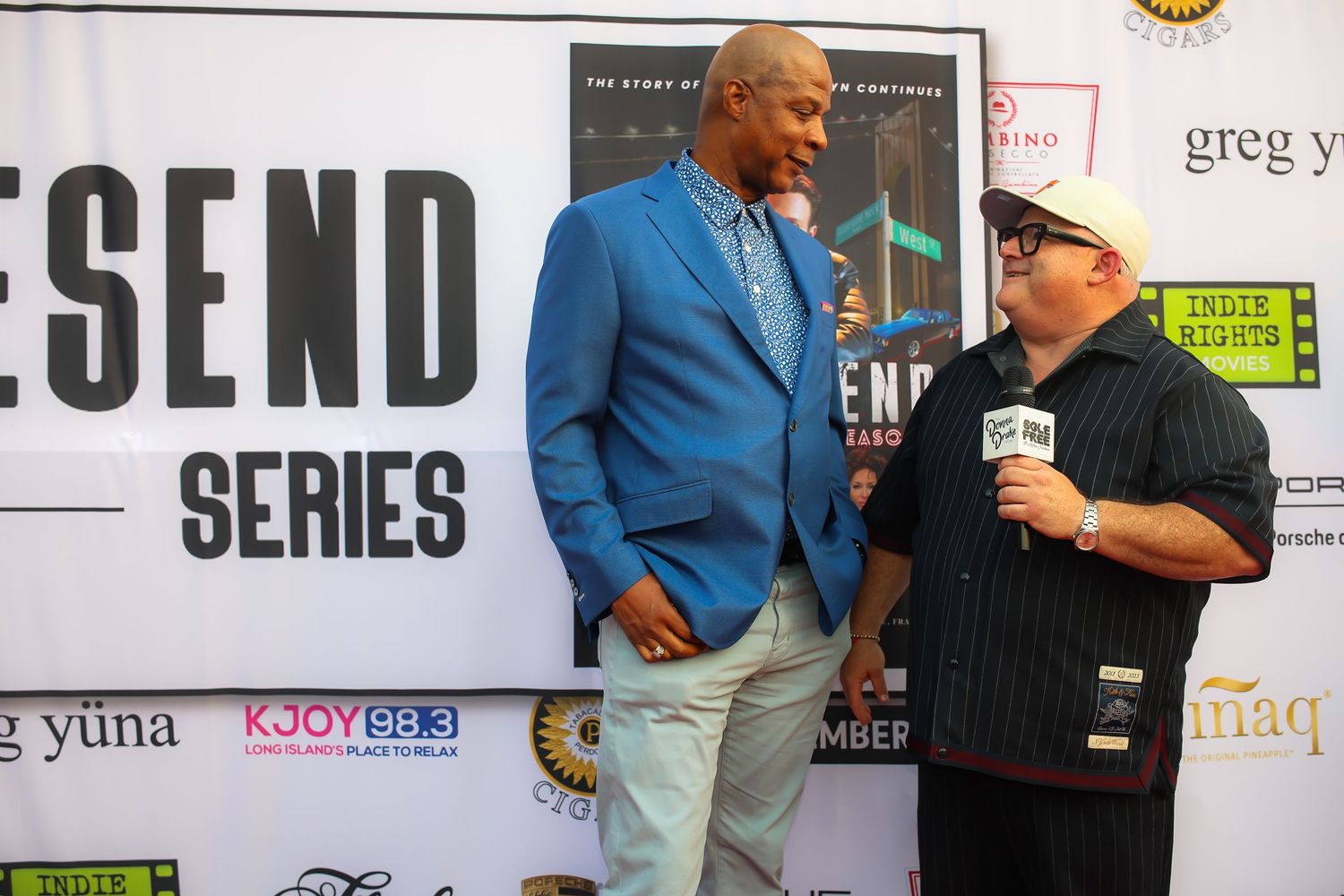 Two people stand together at a media event with a backdrop featuring the word 'SEND' in large letters.