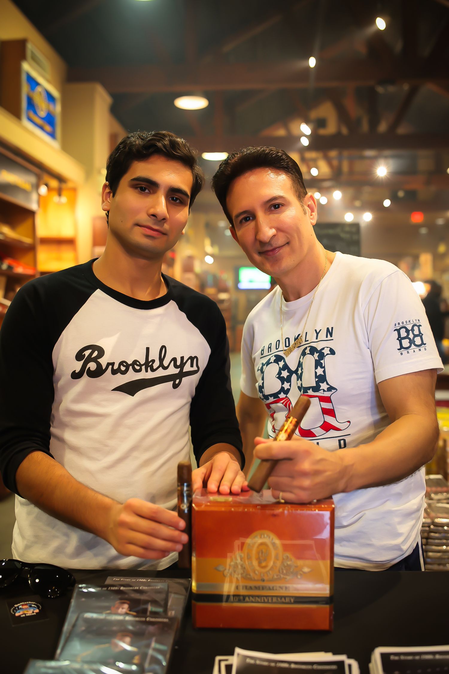 Two people in casual t-shirts pose together at what appears to be a retail counter or merchandise display.
