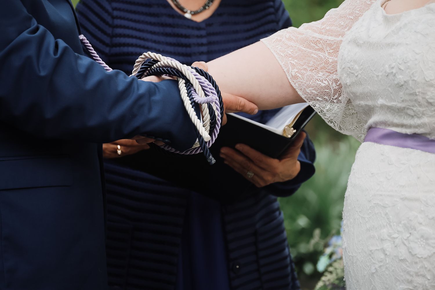 Couple's hands bound together with rope during a handfasting wedding ceremony over a Bible.